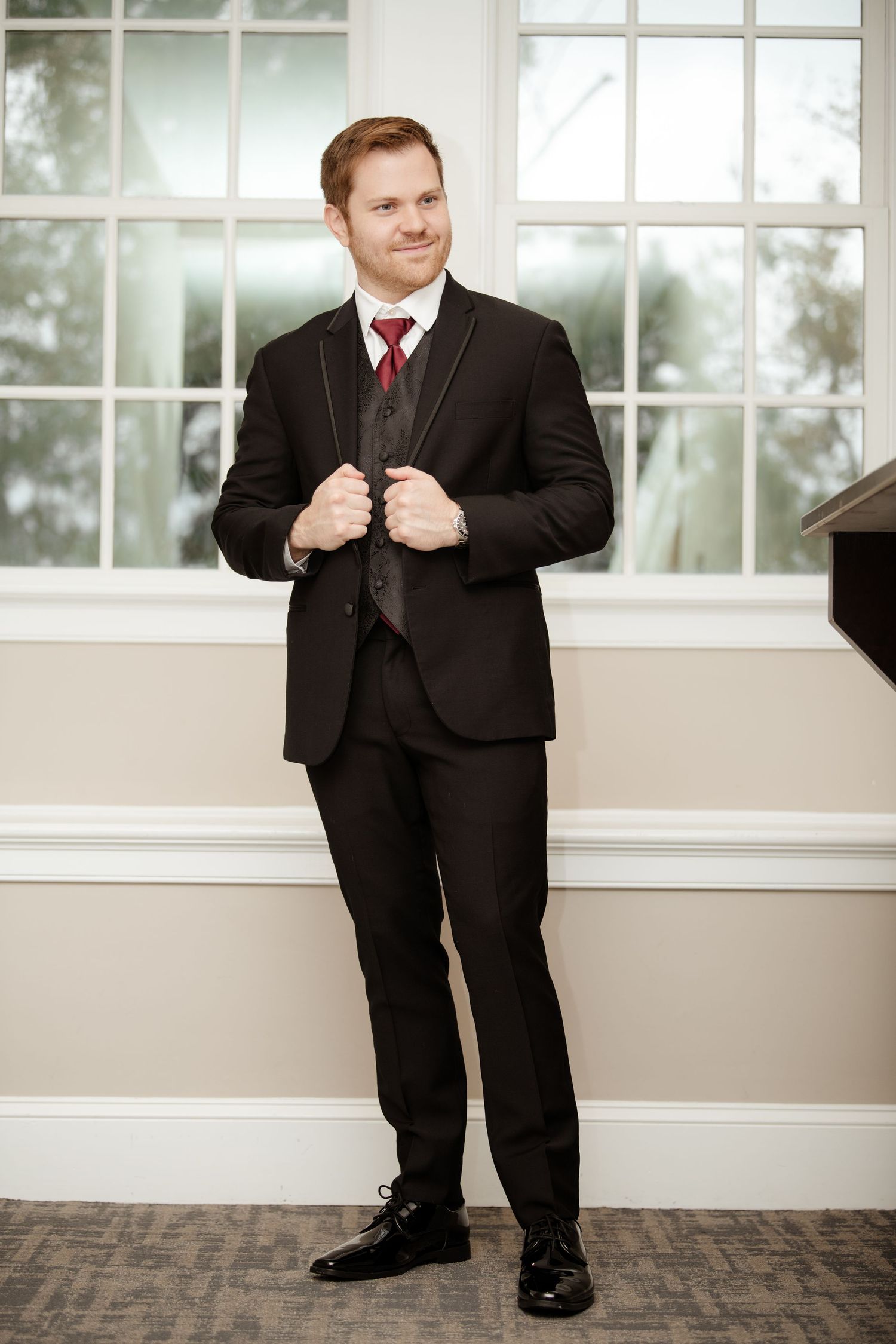 Formal wedding attire with black suit and red tie in elegant indoor setting.
