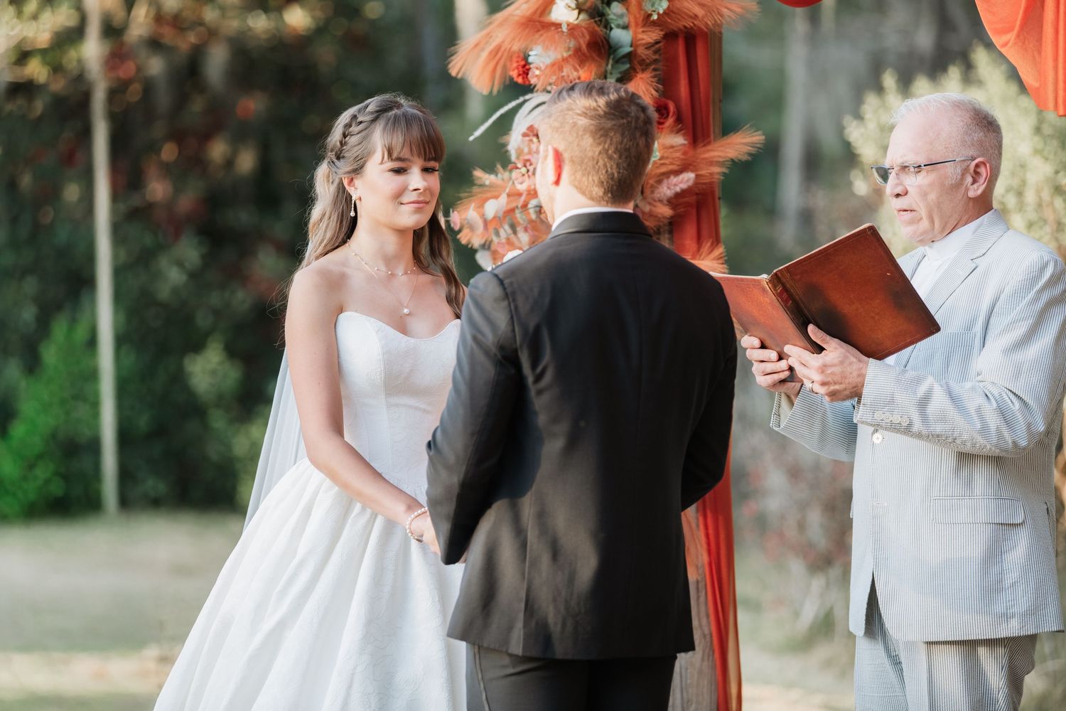 Wedding party gathers under coral-draped pavilion during sunset ceremony.