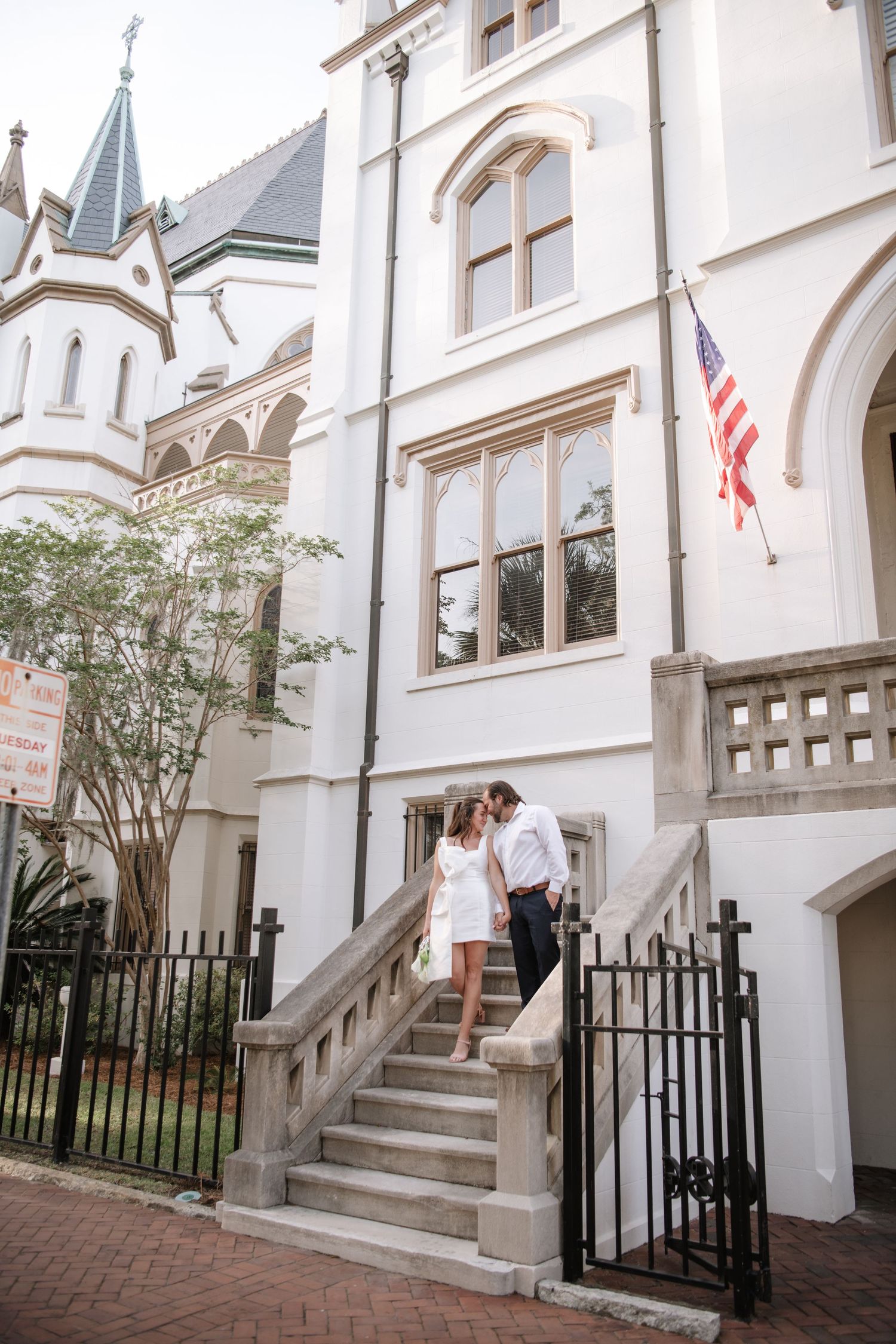 White townhouse with black iron railings and brick walkway features classic architectural details and American flags.