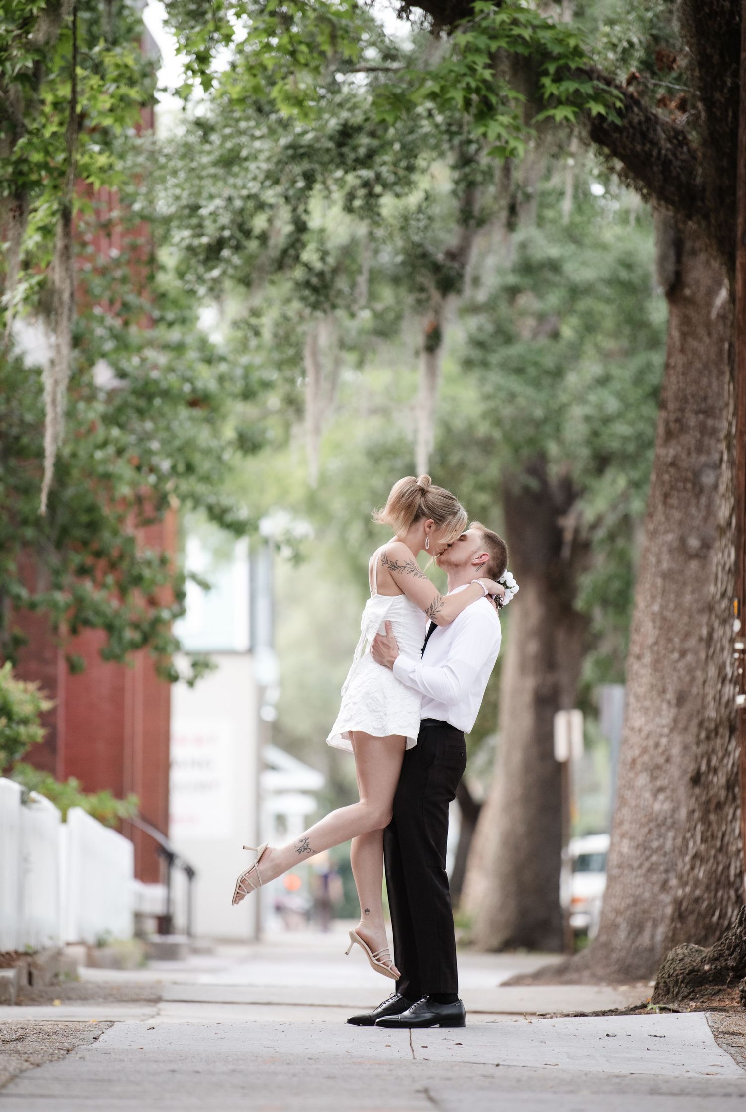 Romantic dance poses on tree-lined street in formal wedding attire.