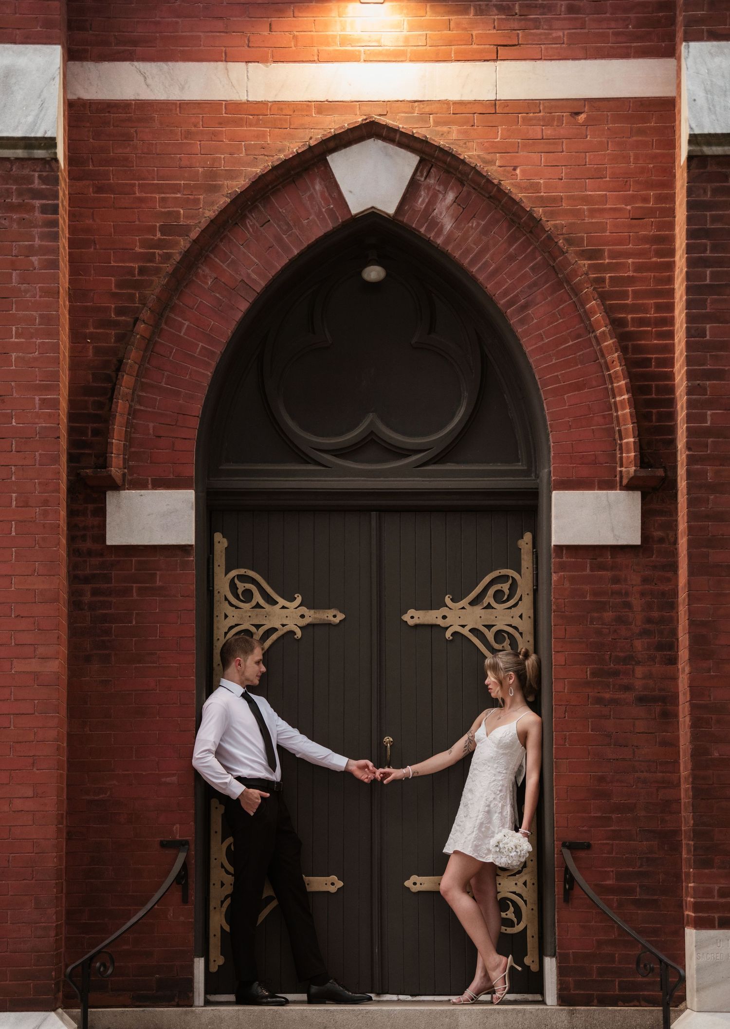 Romantic dance pose in front of red brick building with decorative archways.