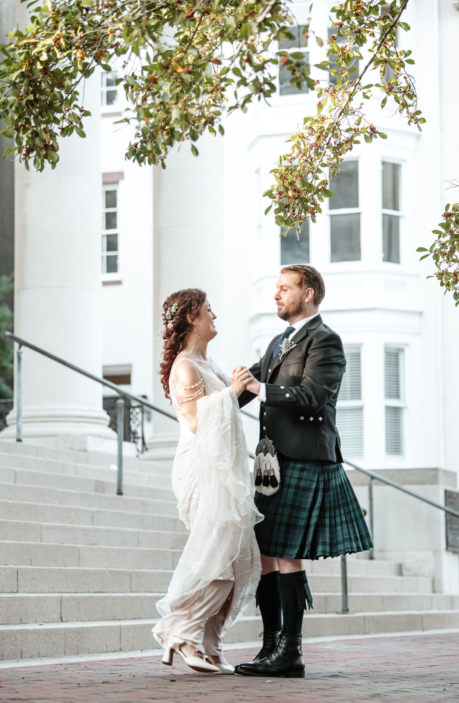 Wedding couple in playful poses on white steps with autumn foliage overhead.