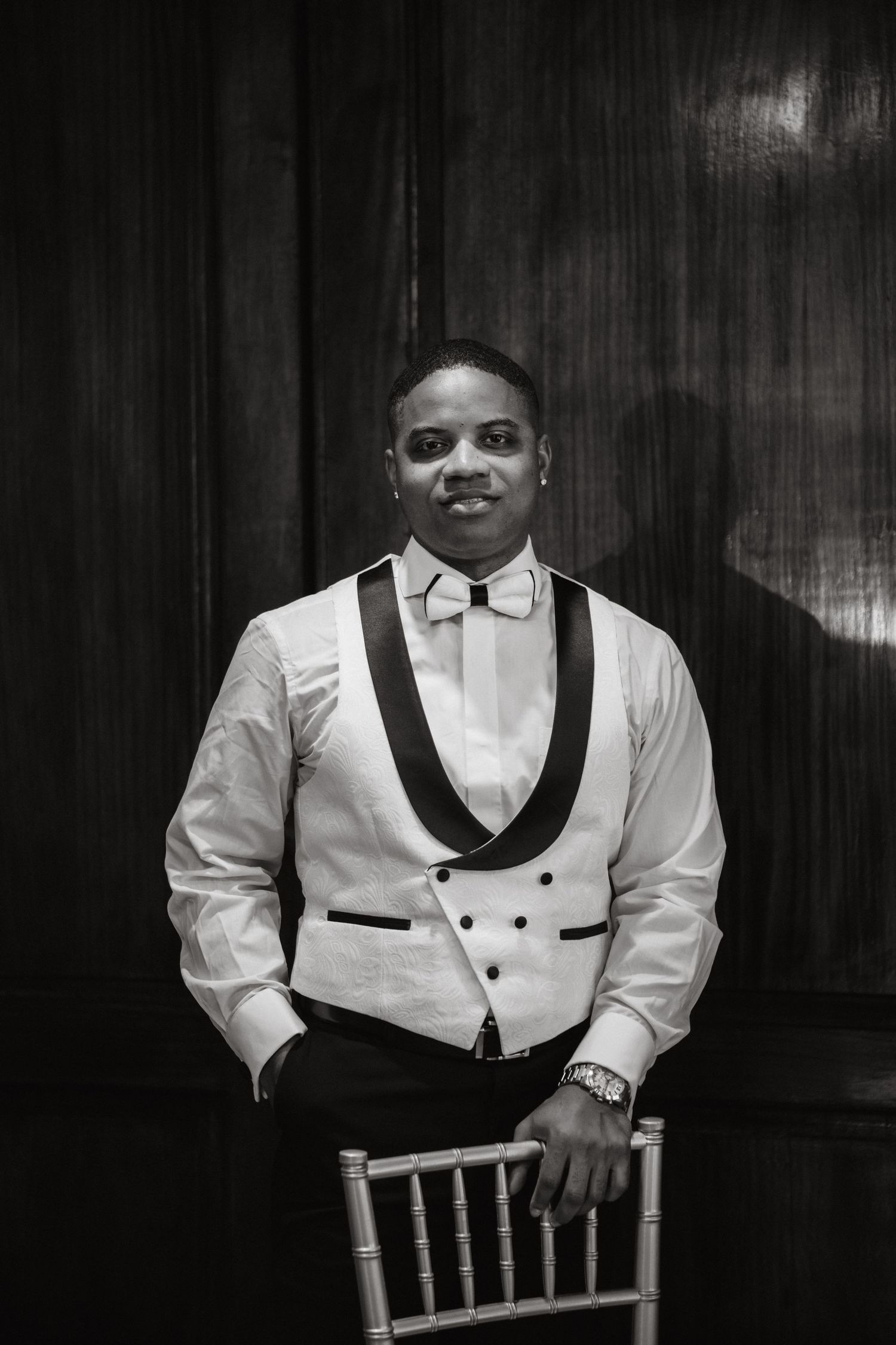 Black and white portrait series of groomsman in white dinner jacket seated on chair.