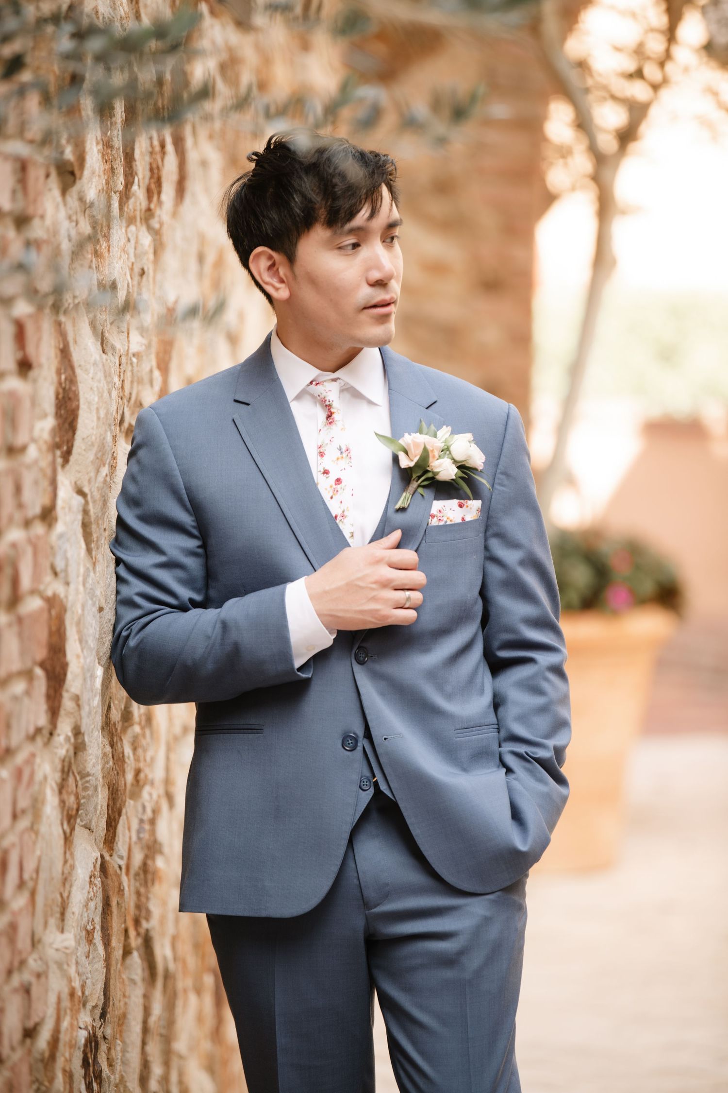Groom in classic grey suit poses thoughtfully against stone pillars.