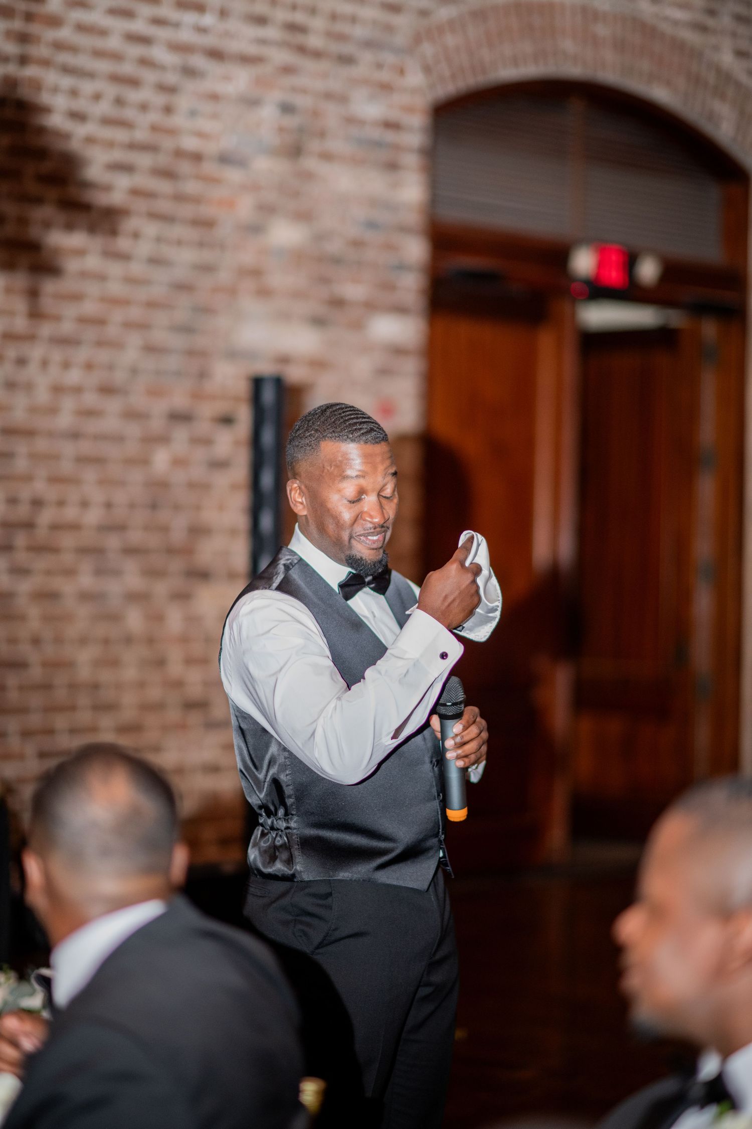 A speaker delivers remarks during a formal event in a brick-walled venue.