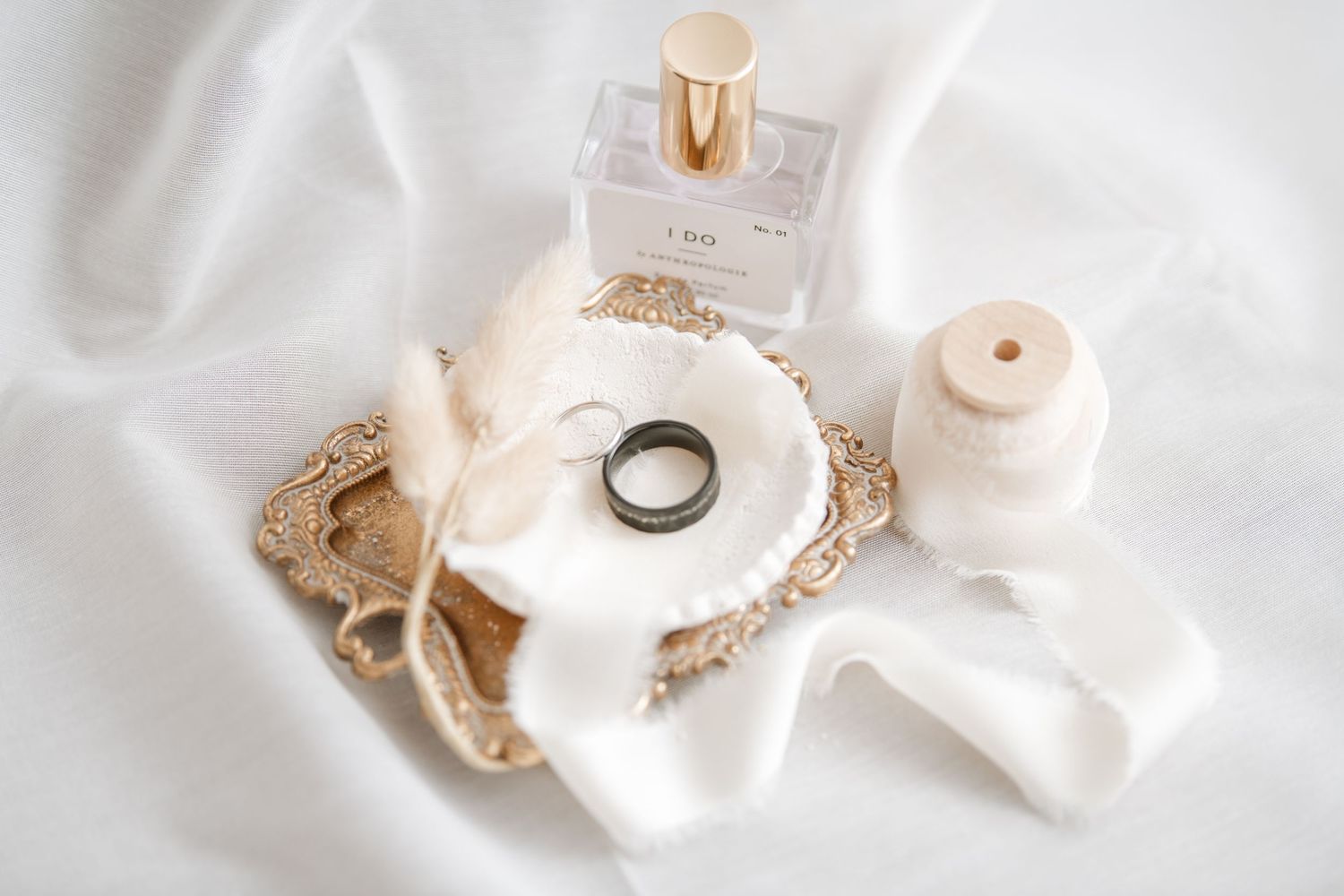 Wedding details flatlay with perfume bottle, ring, and white decor elements on light background.