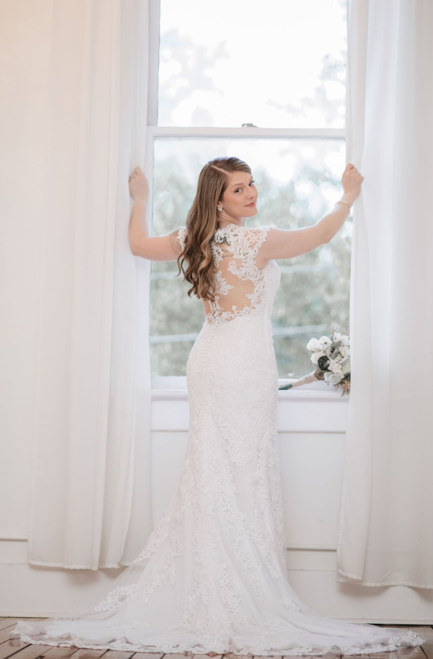 Elegant white wedding gown showcased in bright sunlit room with flowing curtains.