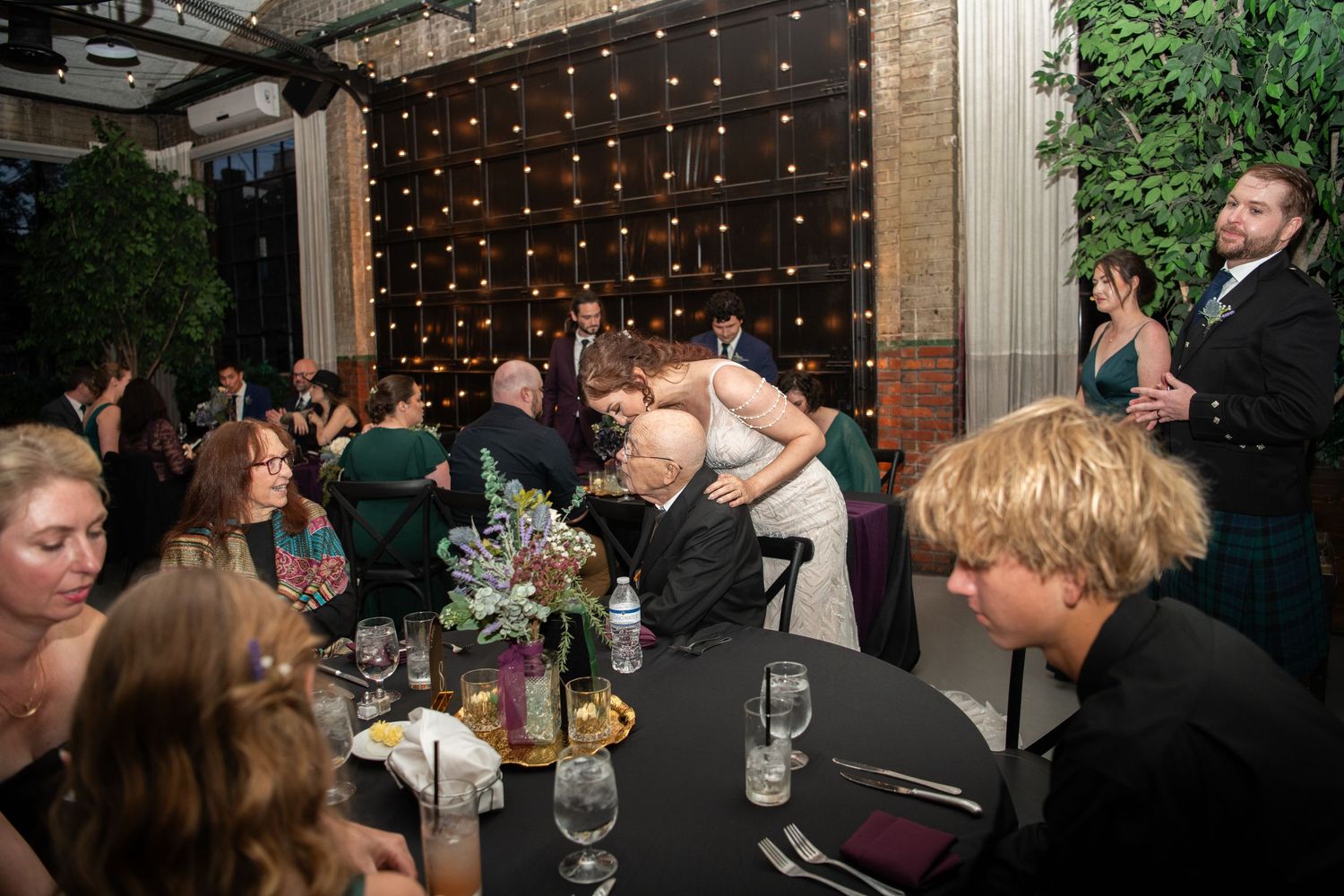 Wedding guests mingling at an evening reception with string lights and greenery decorations.