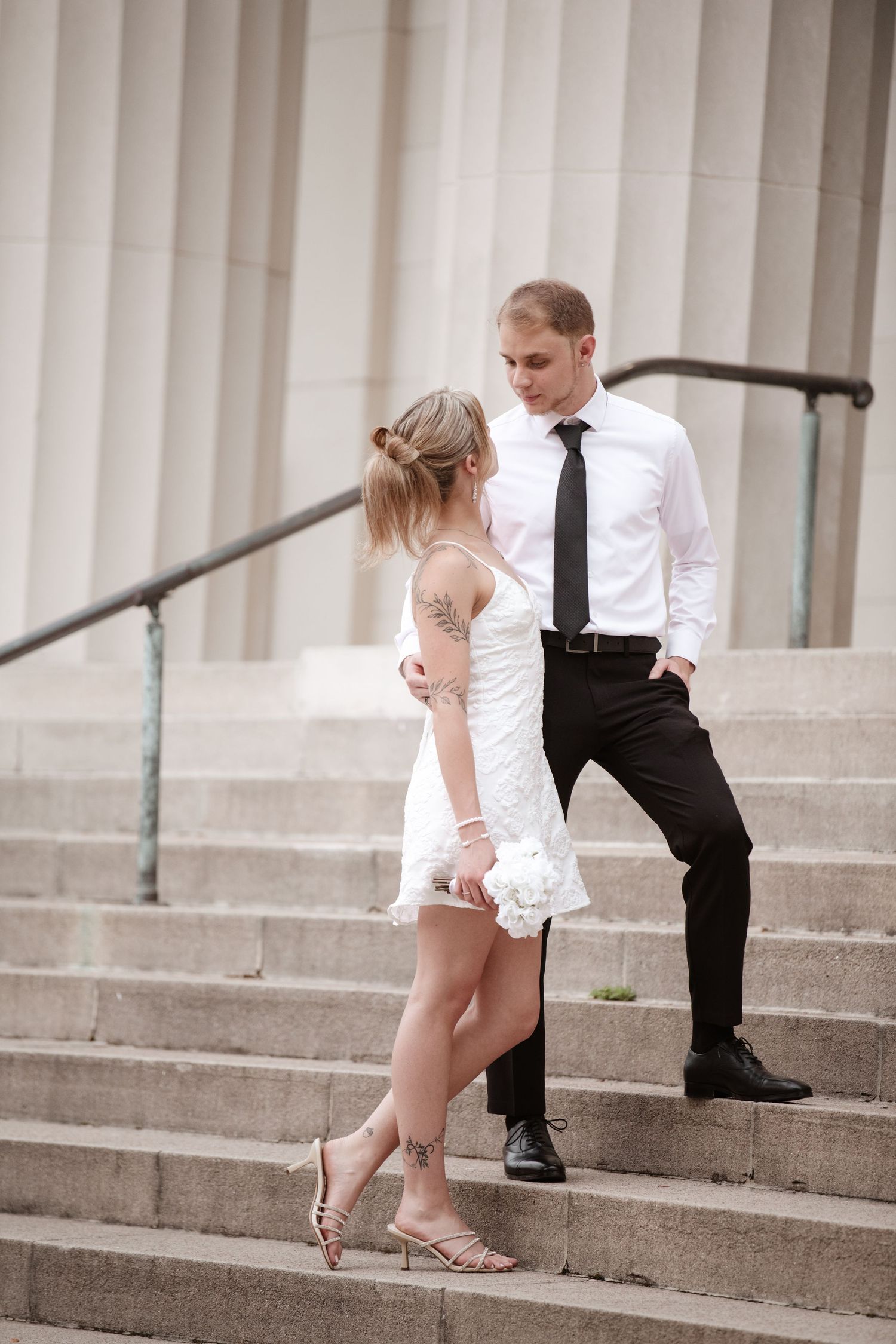 Elegant couple poses on stone steps against white columned backdrop.