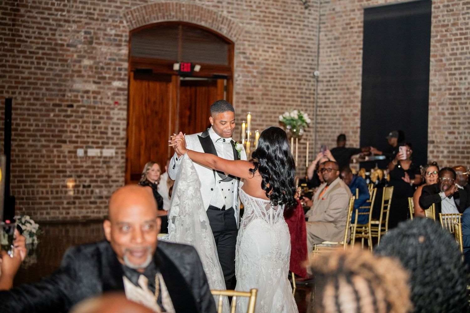 Wedding reception crowd mingling and dancing in industrial brick venue.