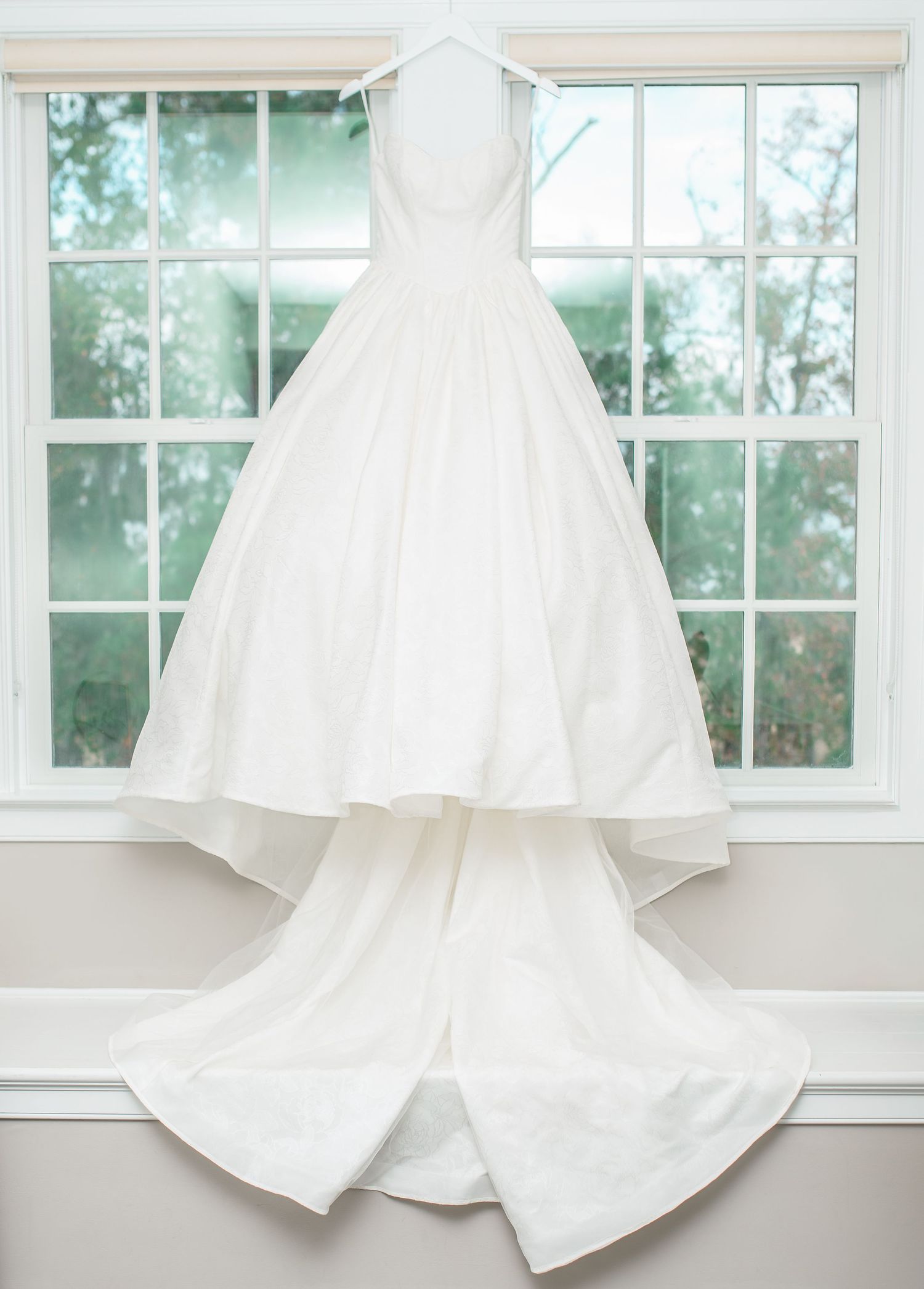 Multiple white wedding dresses displayed against bright windows in bridal boutique.