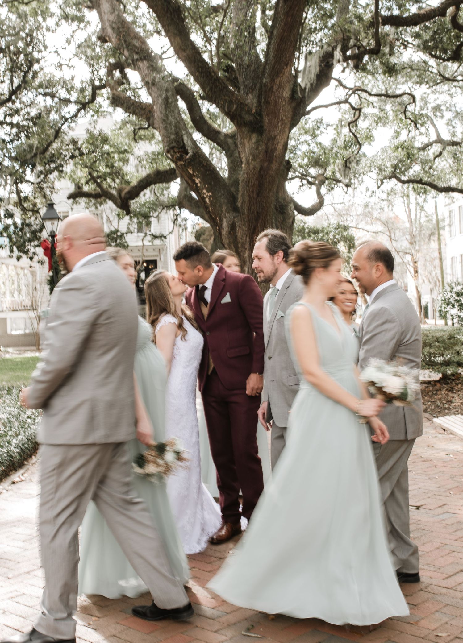 Wedding party celebrates with joyful dancing and candid moments under oak trees.