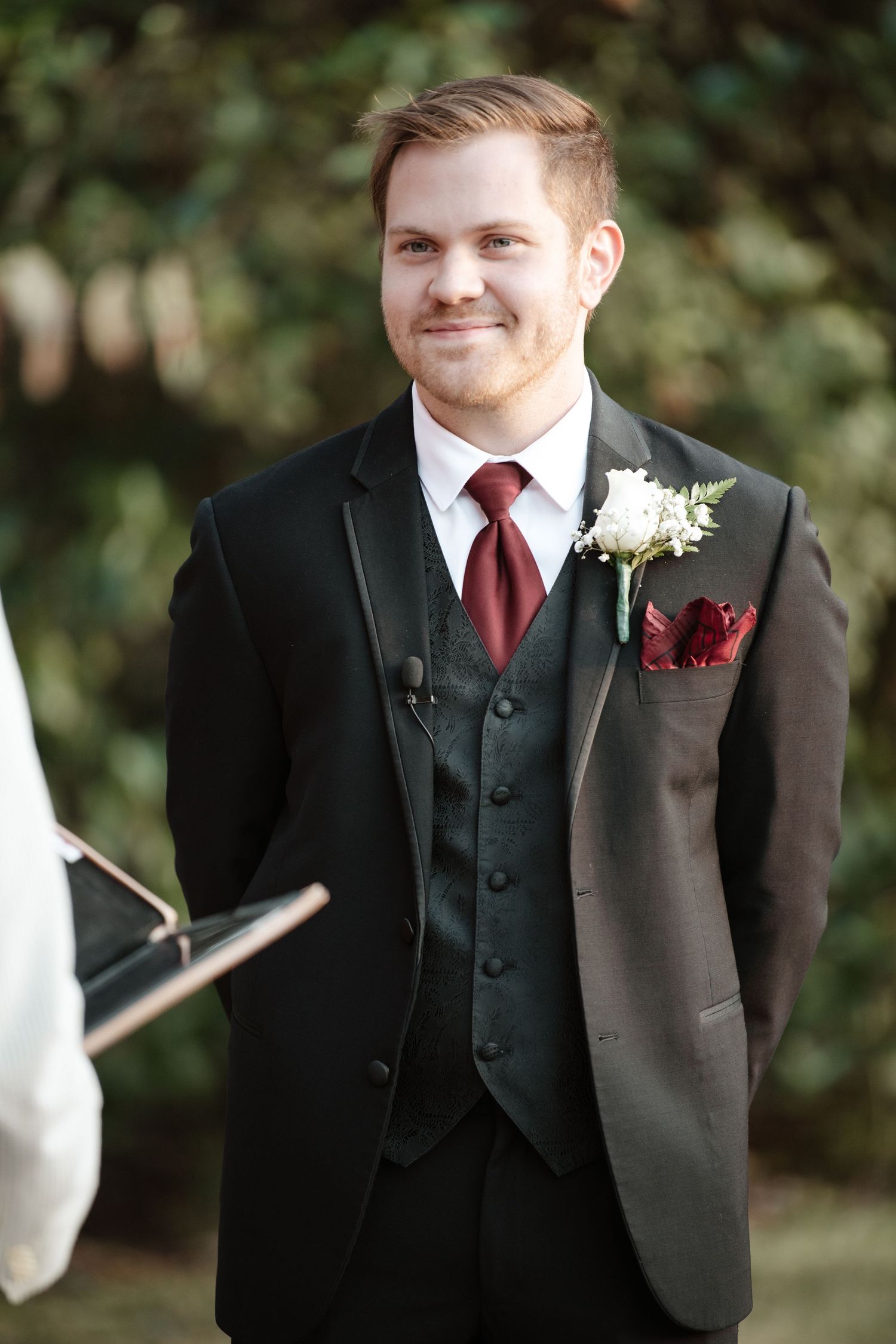 Formal portrait of someone wearing a black suit with burgundy tie and white boutonniere.