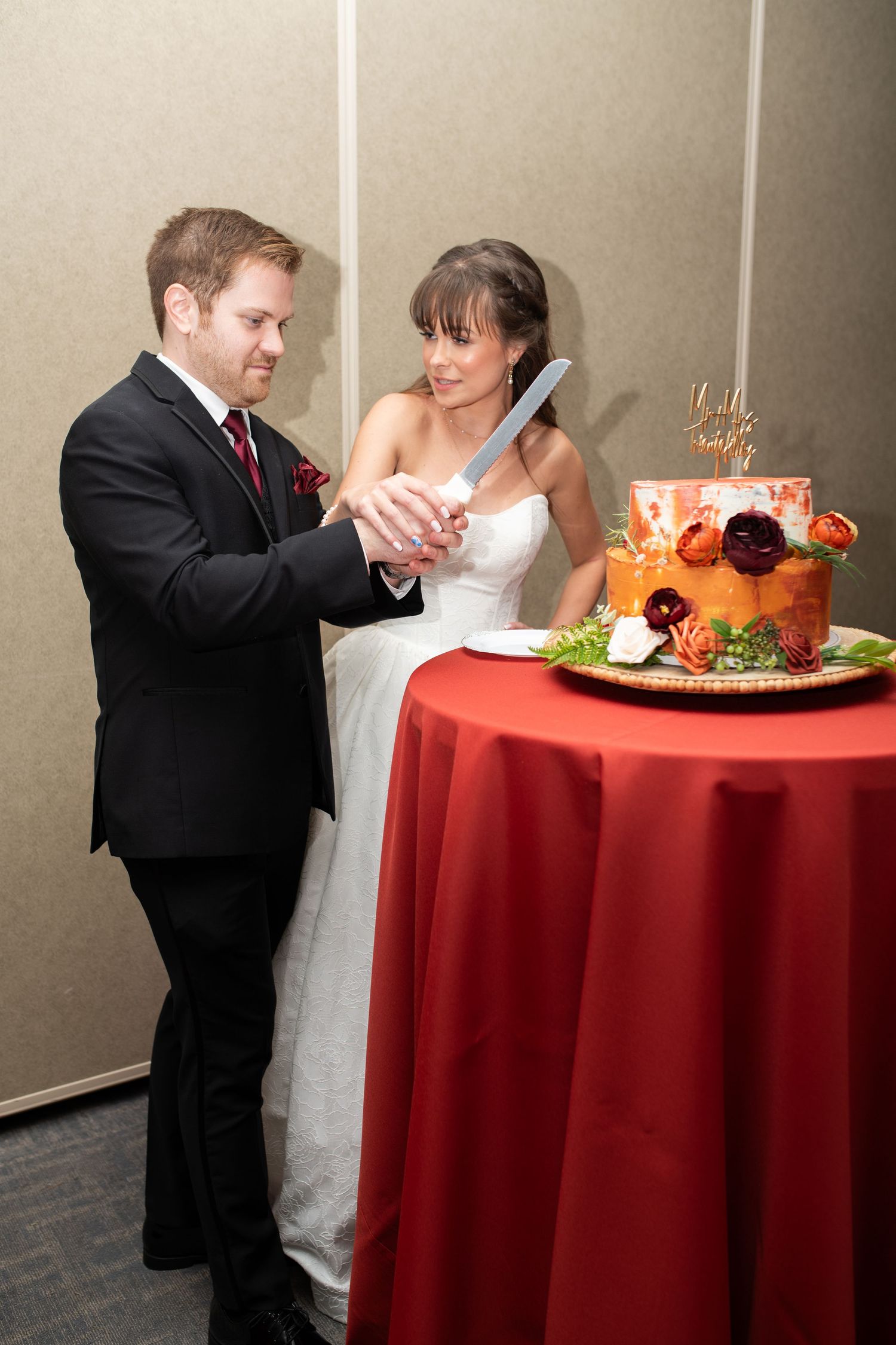 A couple cuts their orange and red decorated wedding cake together at their reception.