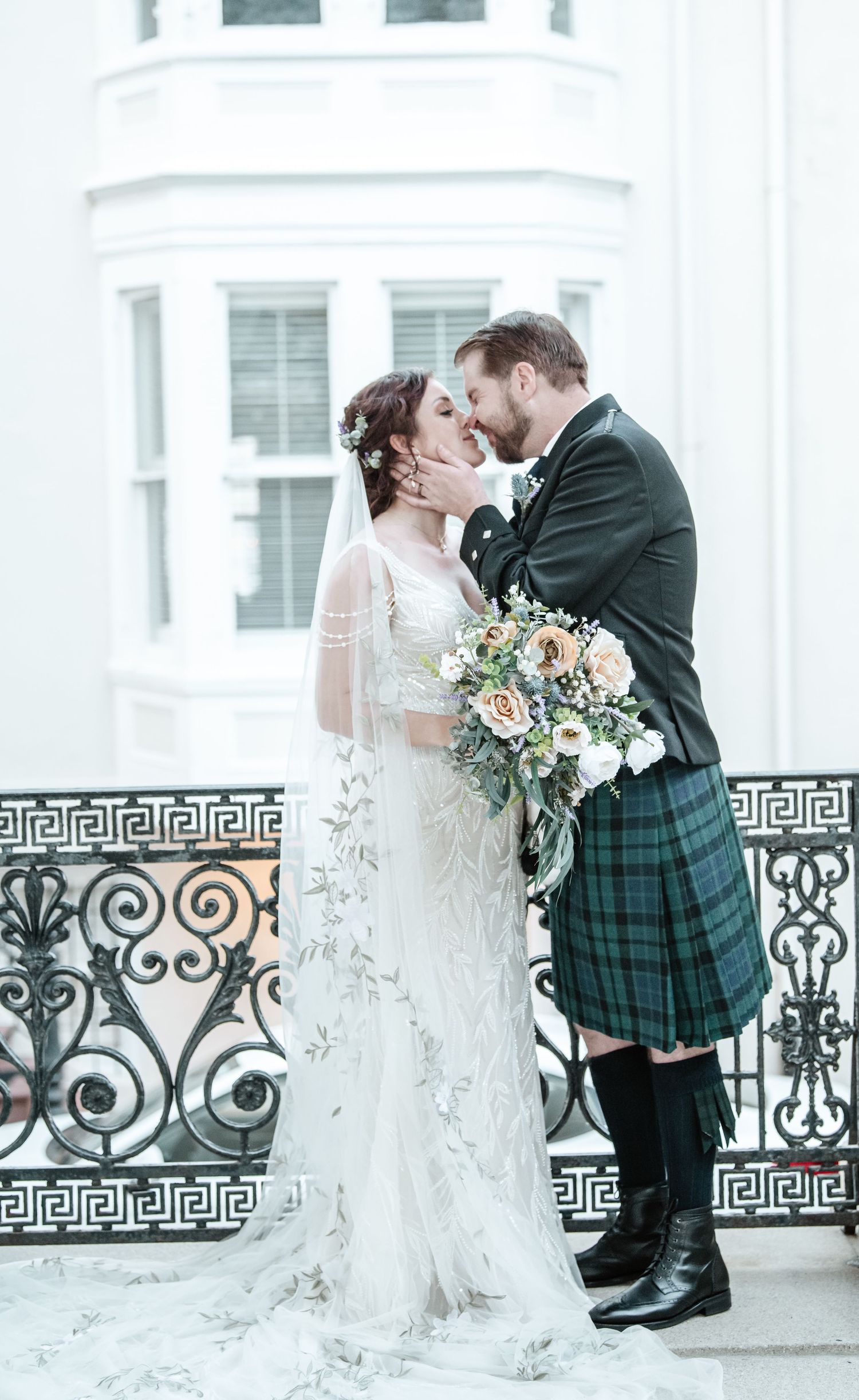 Scottish wedding couple sharing intimate moments by ornate iron railing.