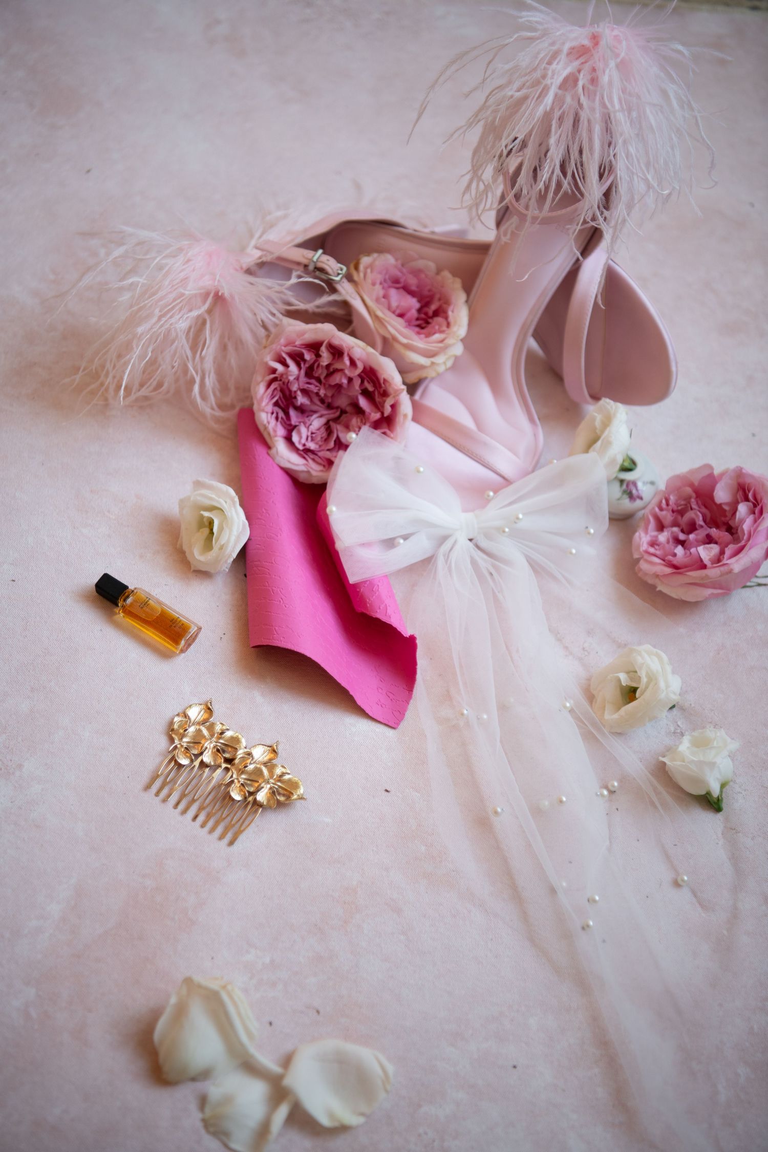Bridal accessories with pink roses, gold crown, and feather details on blush background.