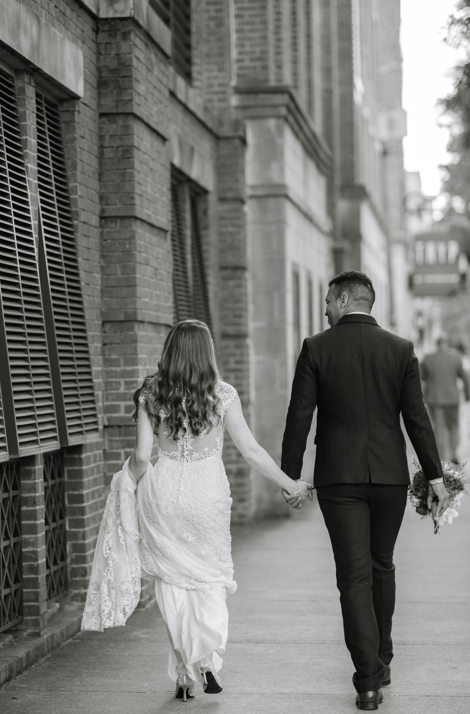 Black and white photo of a couple walking hand in hand down a historic brick-lined street.