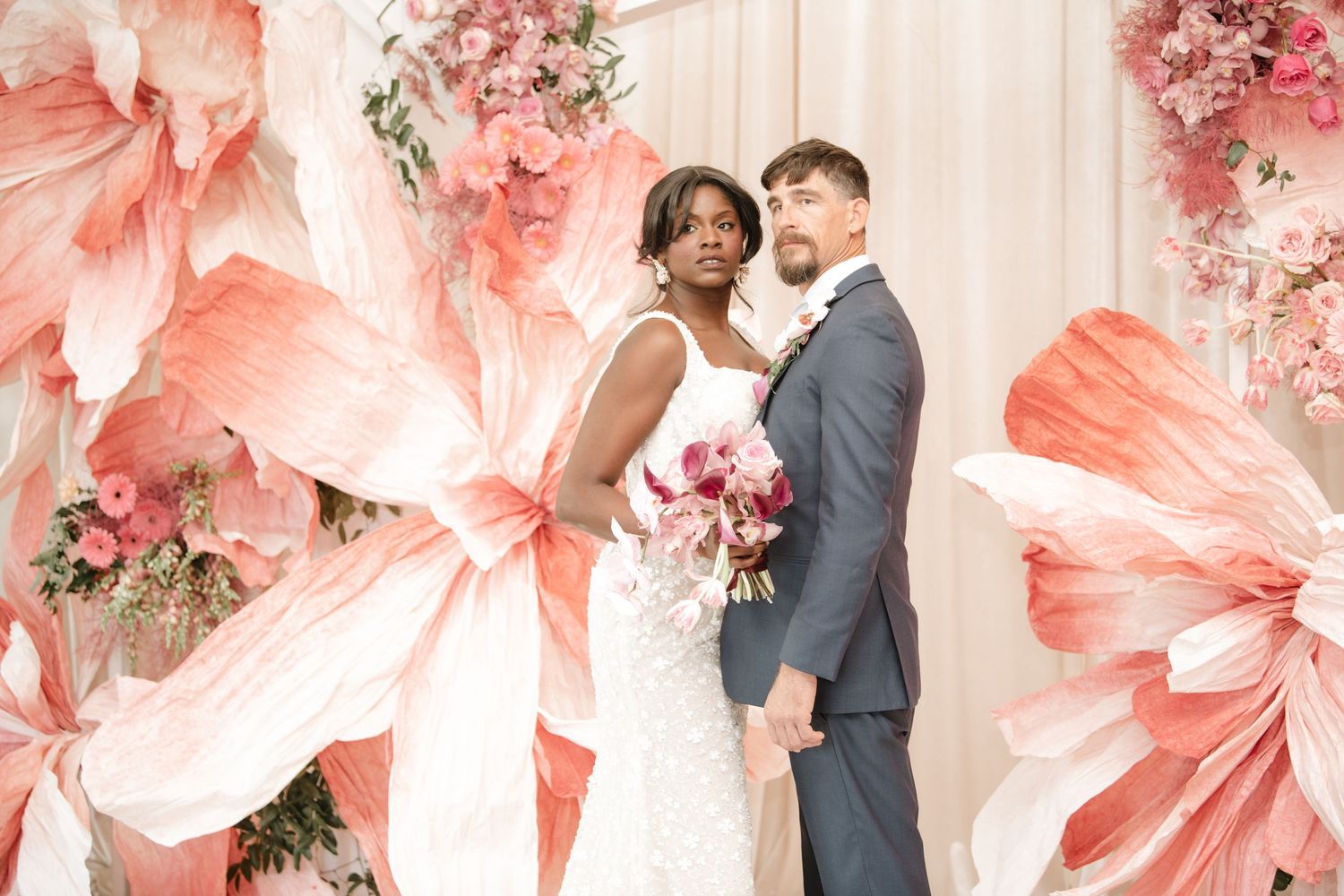 Romantic wedding scene with coral-colored floral decorations and white backdrop.