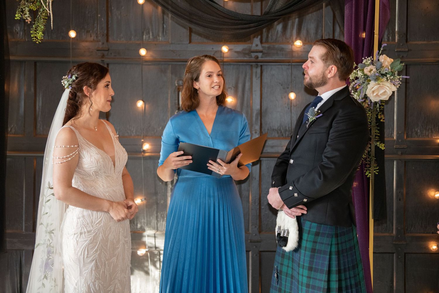 Wedding party members in blue dresses and kilts gather for a celebratory moment.
