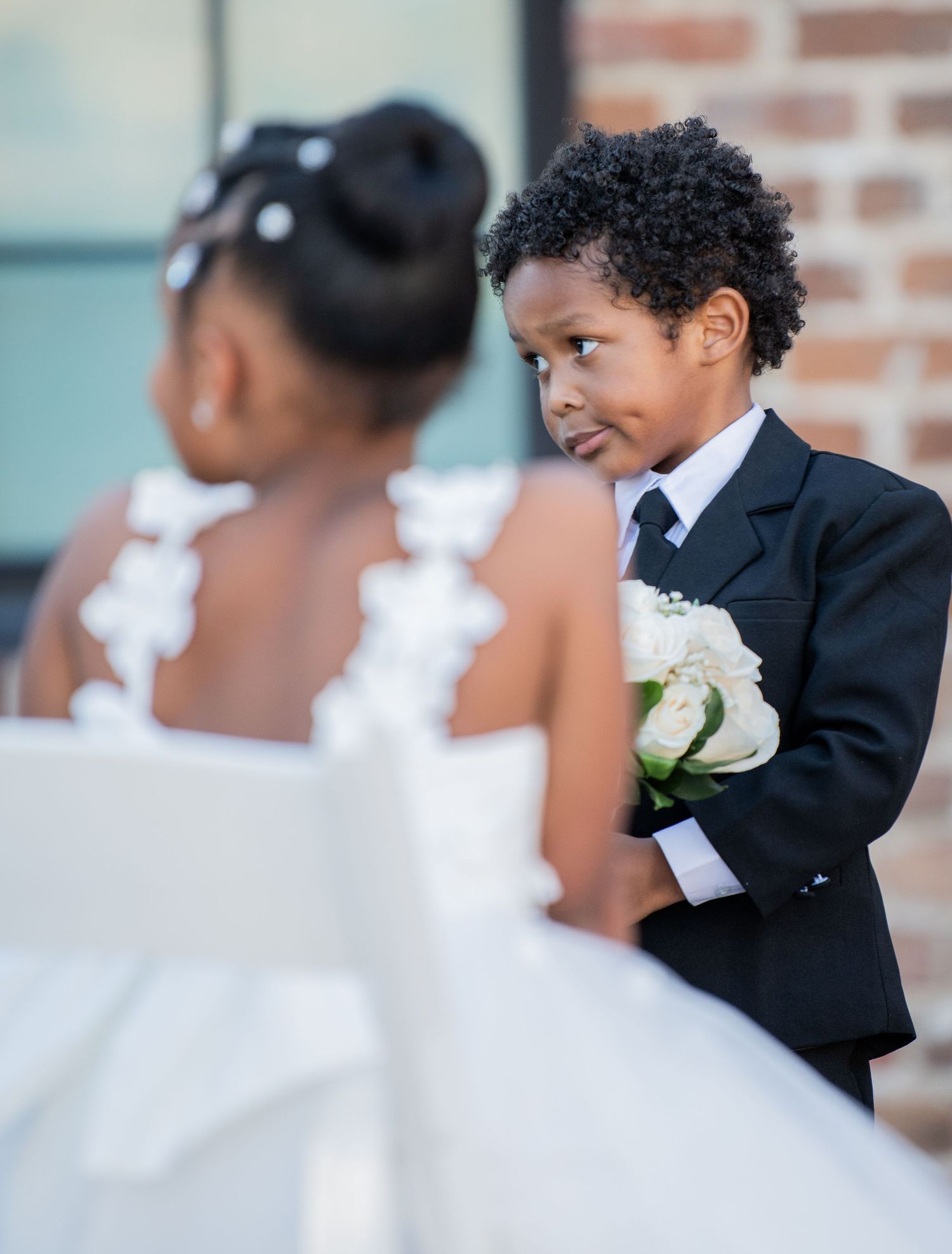 Wedding party members in black and white attire pose against a brick wall during formal photos.