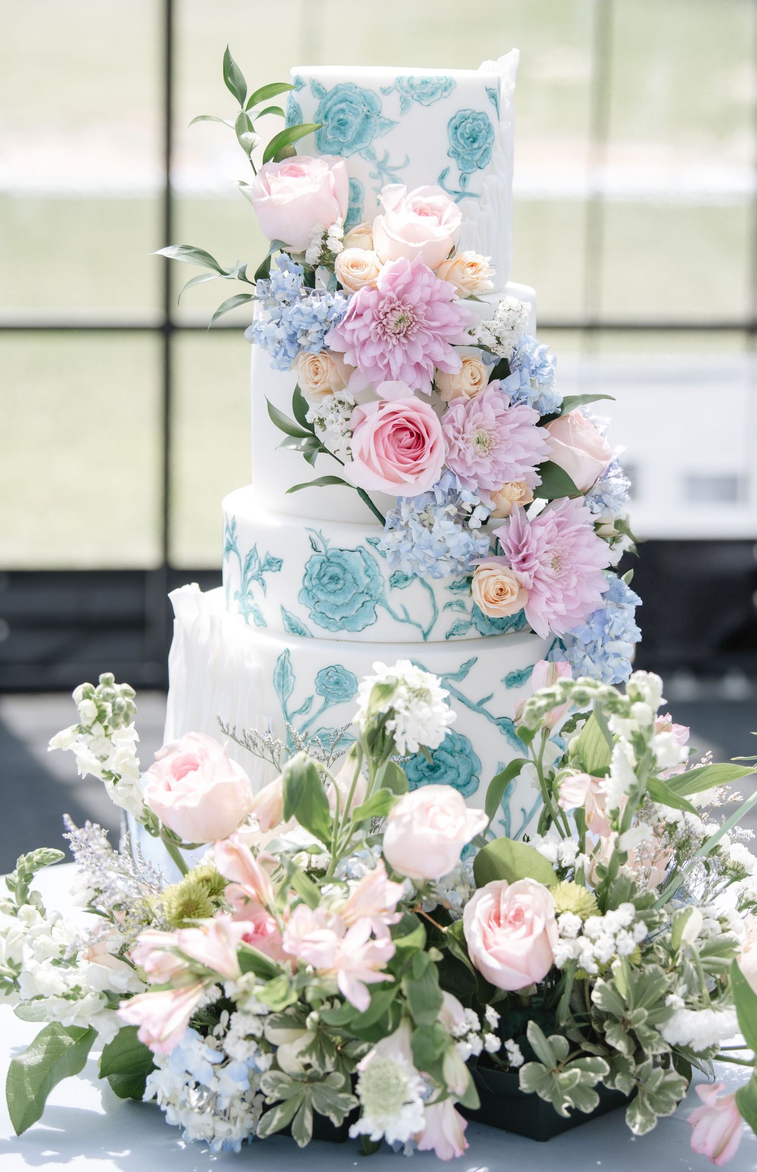 Elegant wedding cake decorated with pastel blue and pink sugar flowers and greenery.