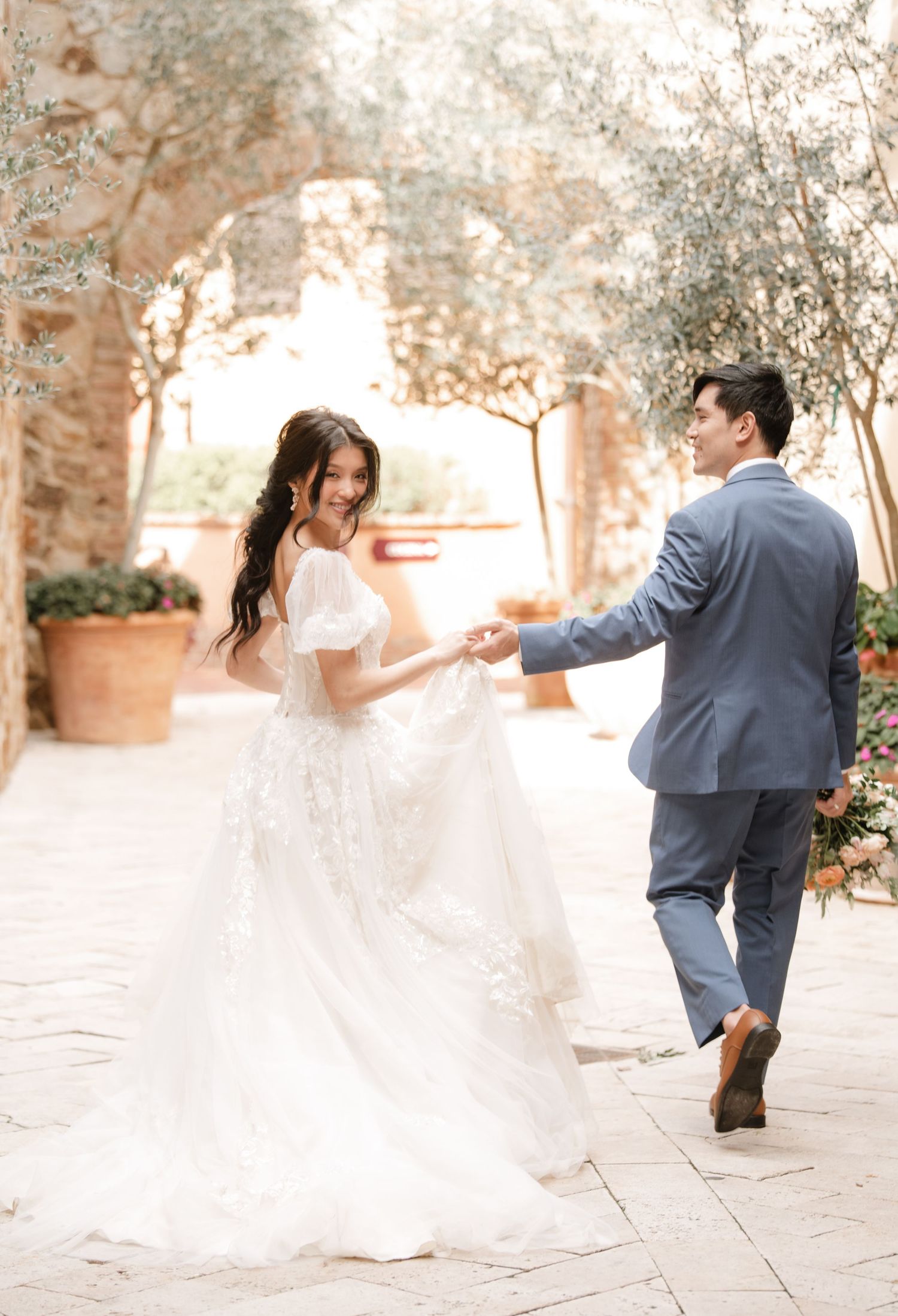 Wedding couple dancing and twirling through a stone courtyard in romantic lighting.