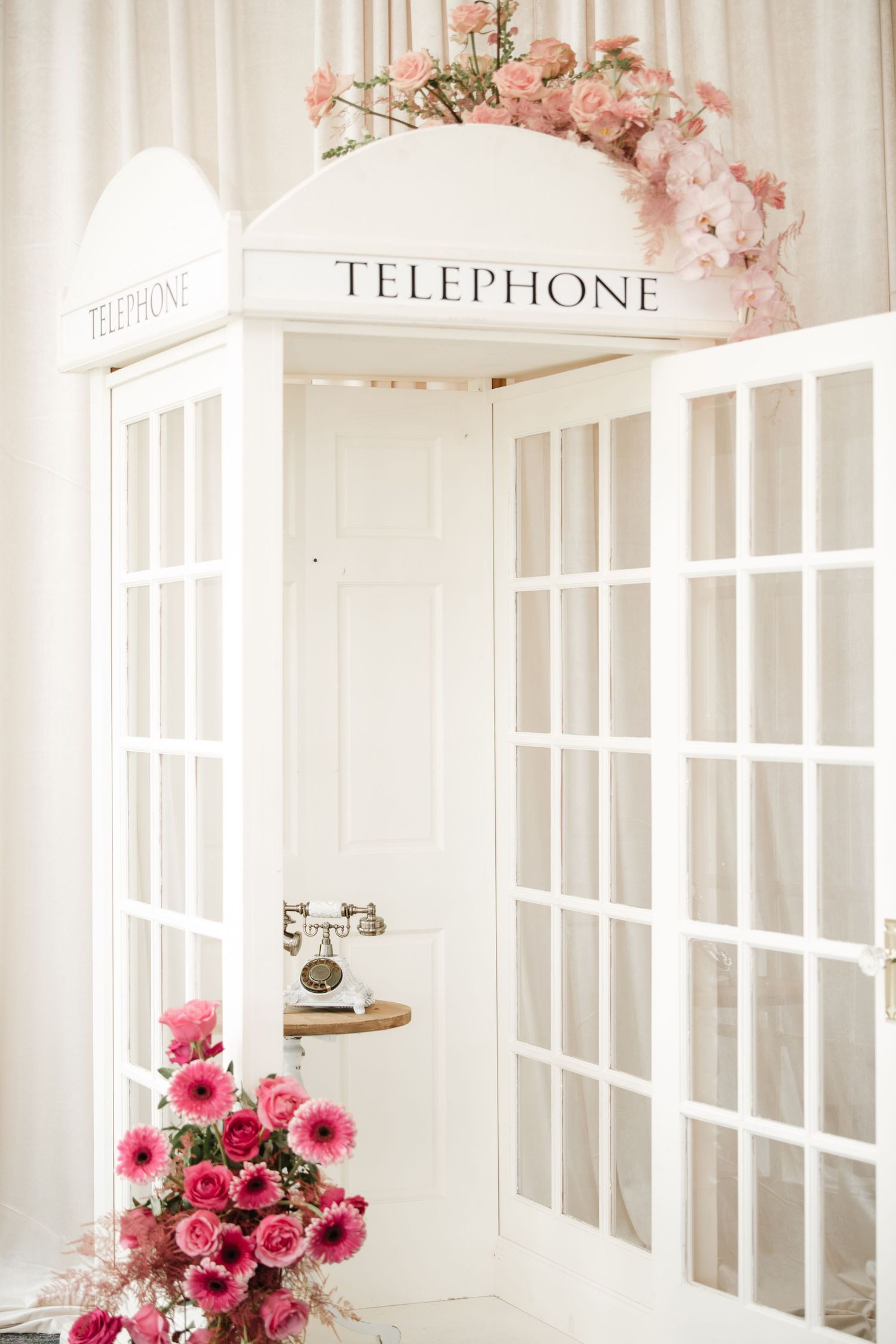 Vintage white telephone booth with pink floral arrangements in an elegant setting.