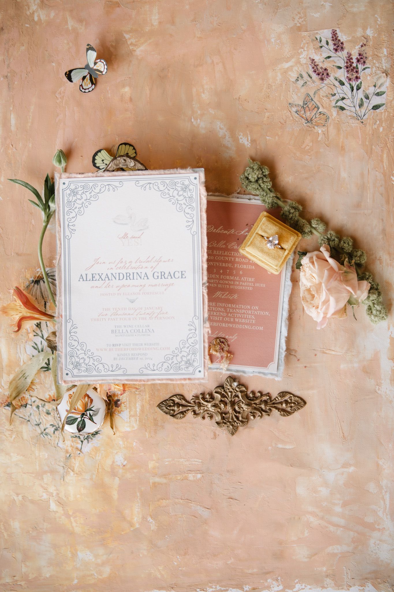 Wedding invitations and floral details arranged on a textured peach-colored surface.