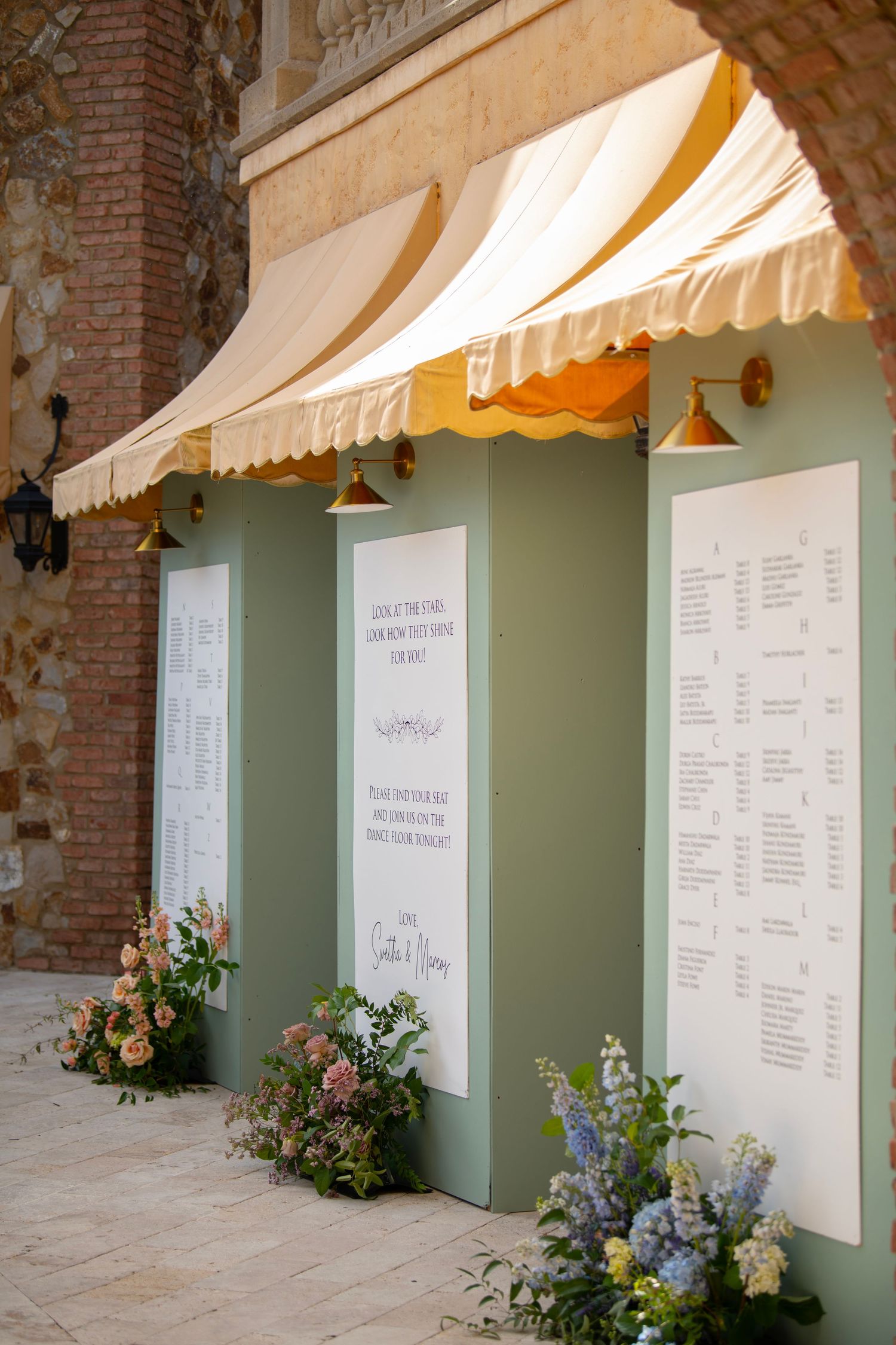 Wedding seating chart display with mint green walls and striped awnings in brick archways.