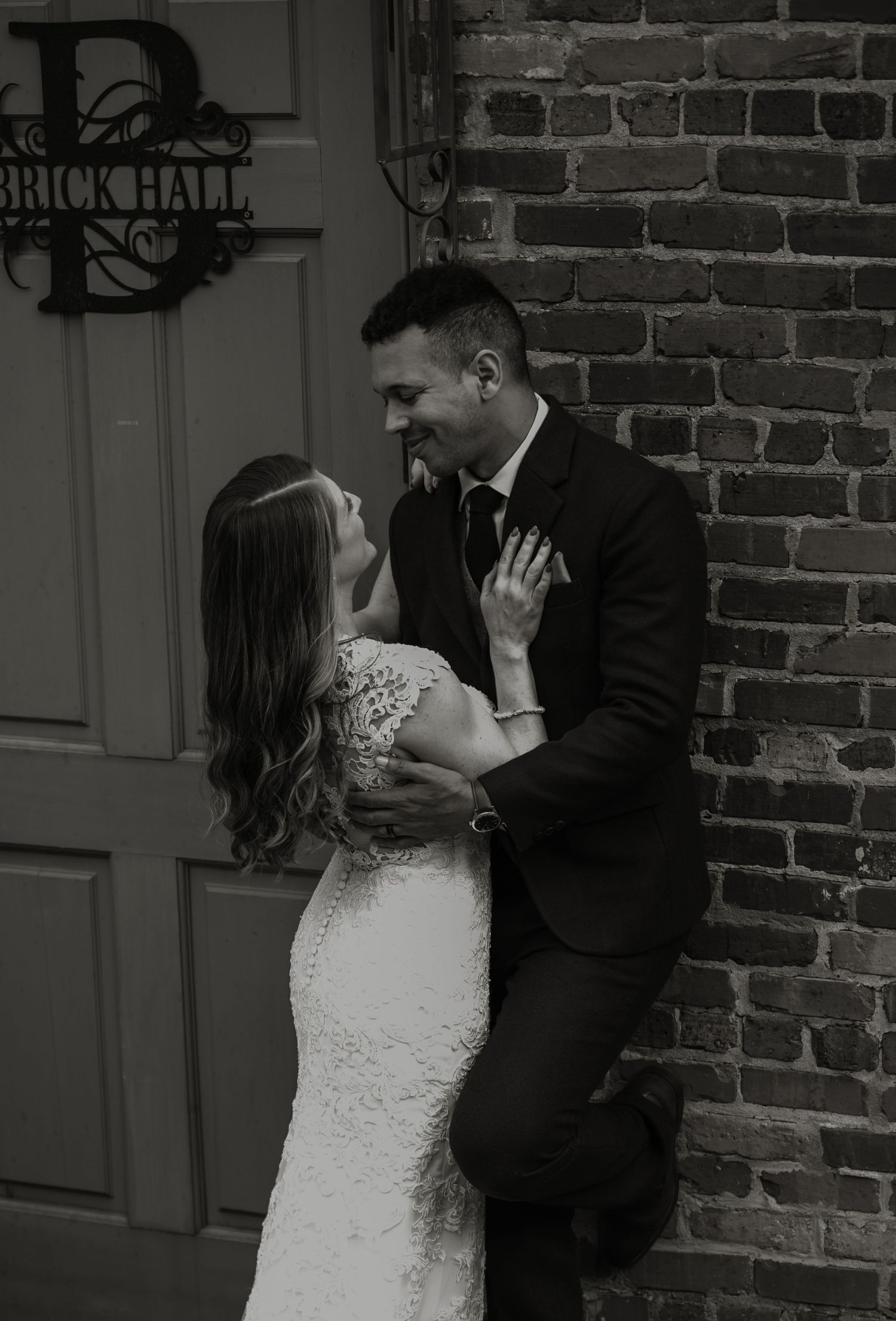 Black and white romantic portraits of newlyweds against a rustic brick wall backdrop.