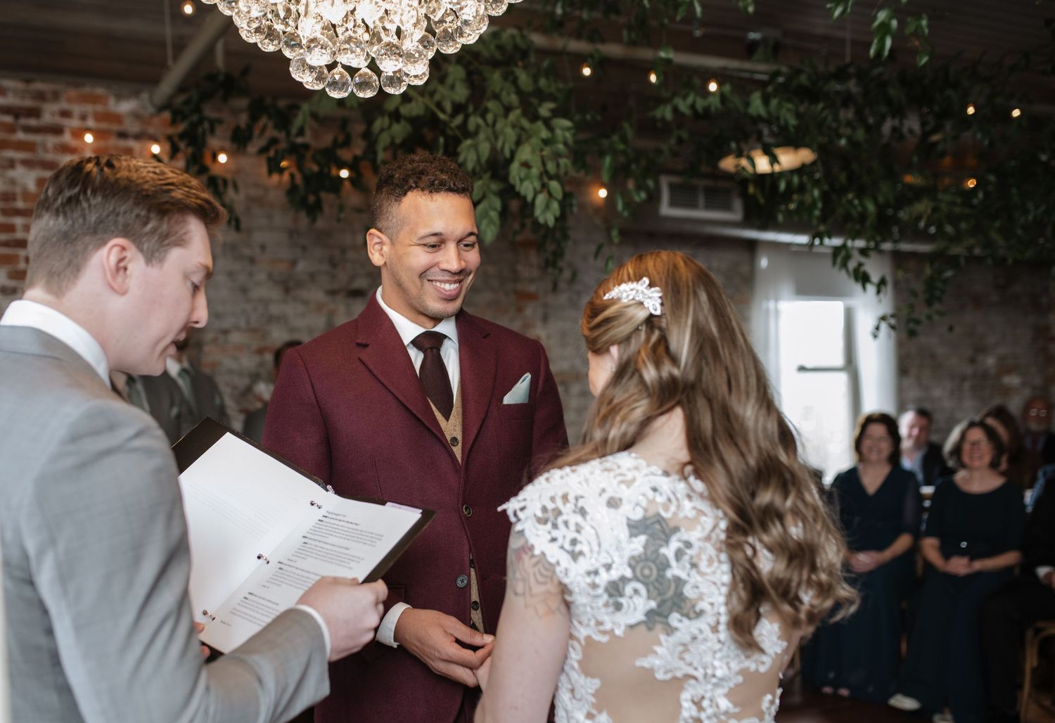 Wedding ceremony participants standing beneath a crystal chandelier in an industrial-style venue.