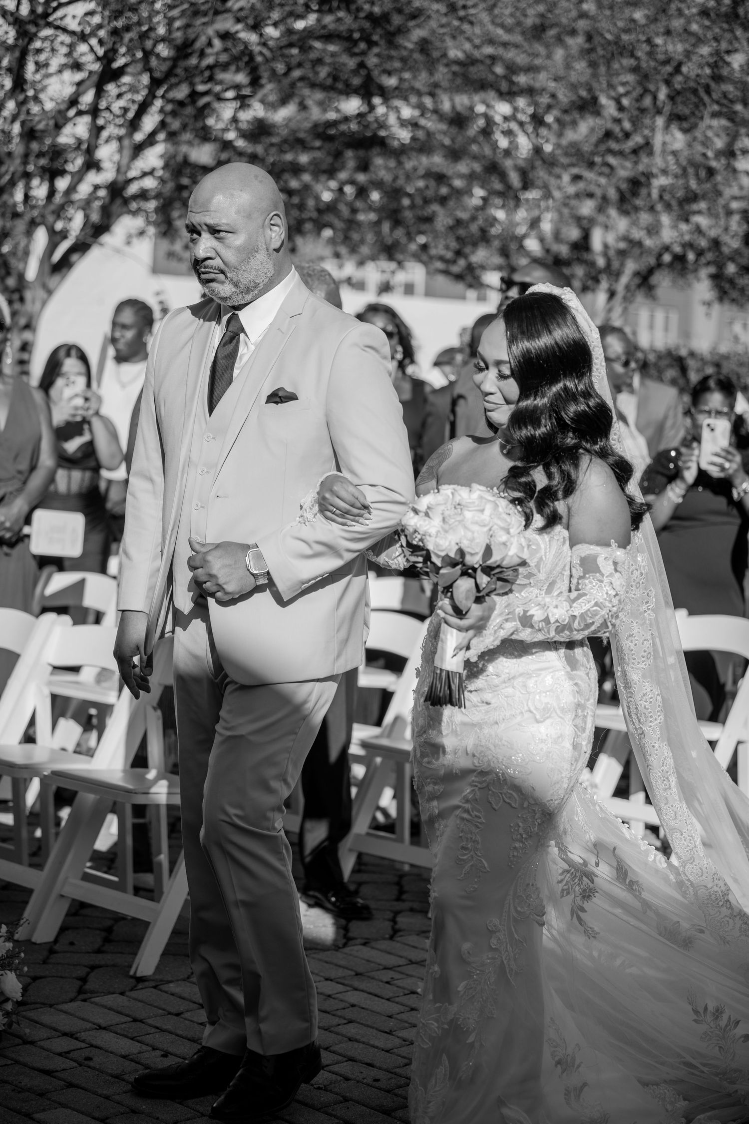 A black and white wedding ceremony photo with guests seated on white chairs in the background.