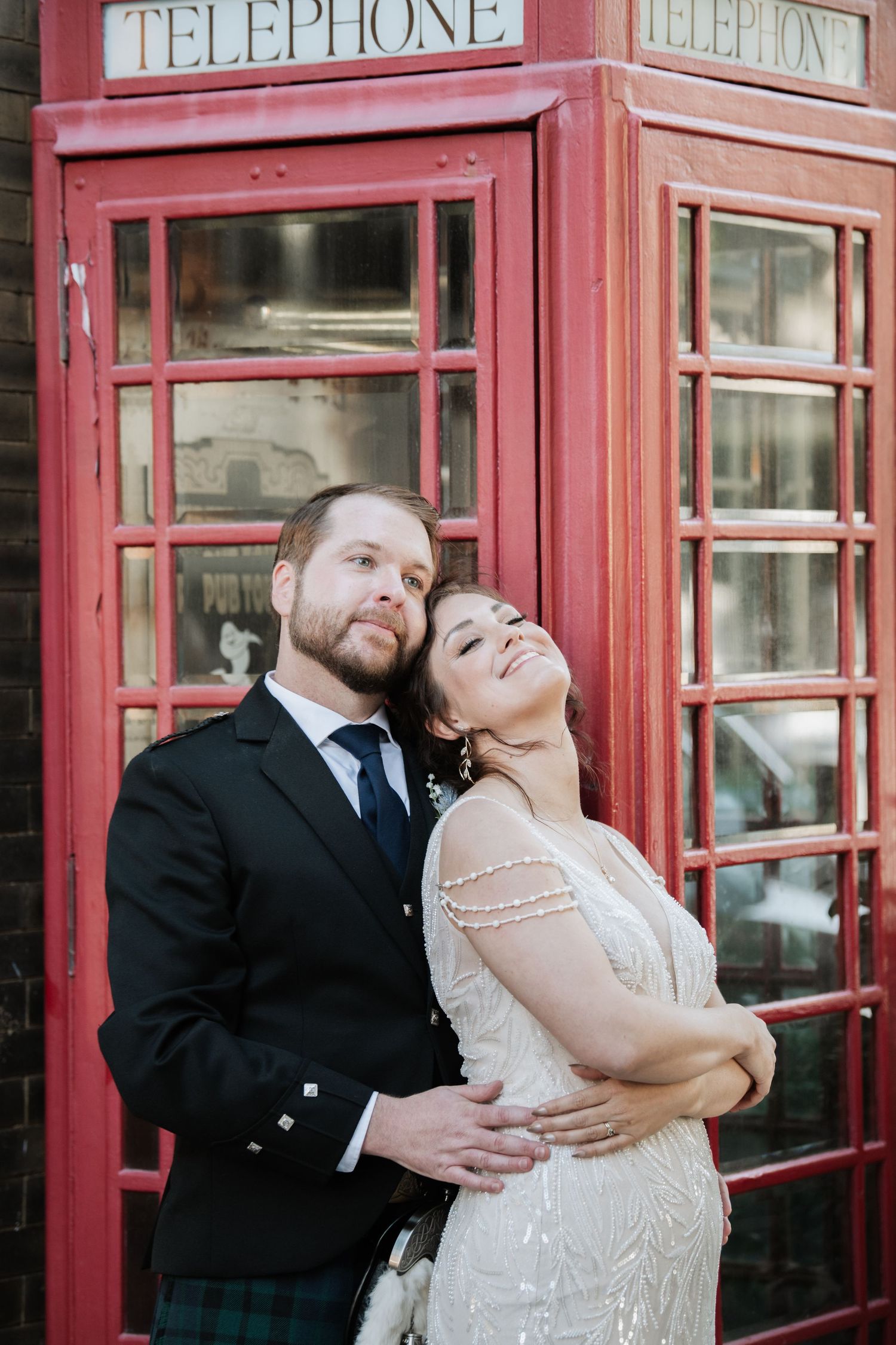 A couple poses playfully in front of classic red British telephone booths.