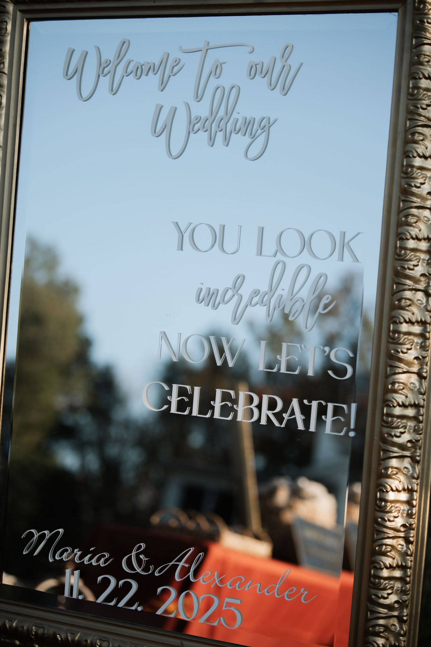 Wedding welcome sign with elegant script text displayed on reflective glass surface.