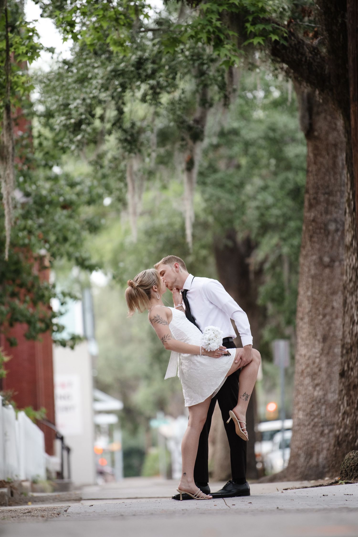 Romantic dance dip sequence on sidewalk beneath Spanish moss trees.