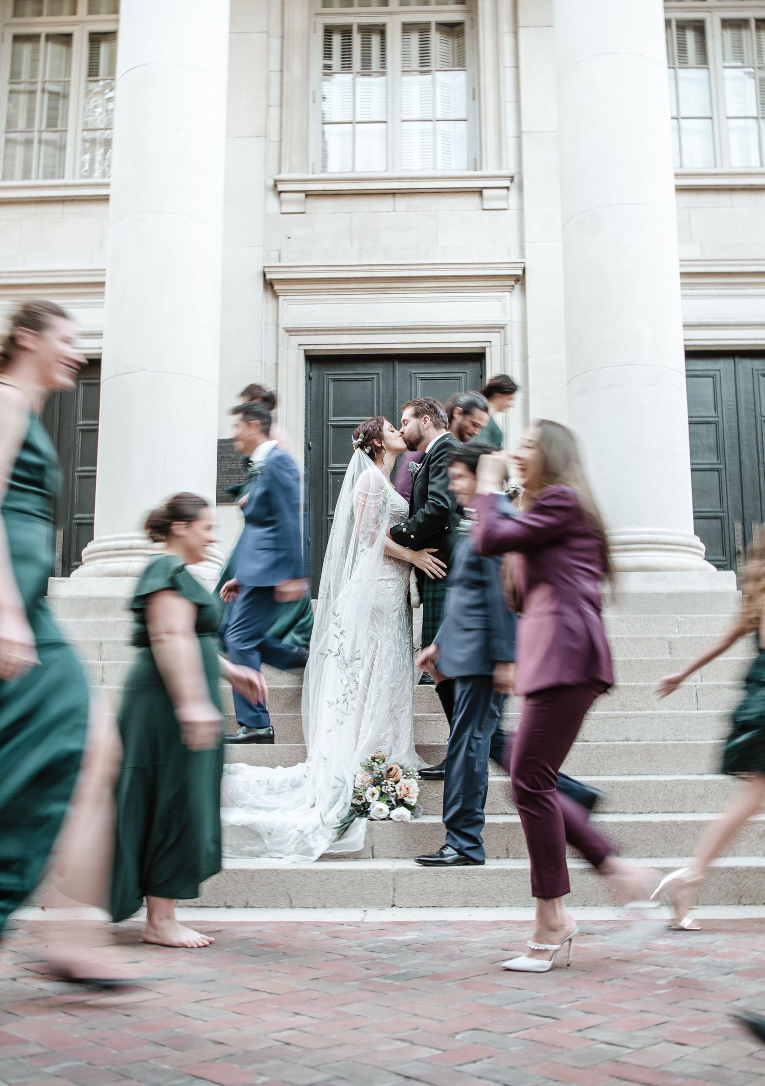 Motion blur of people walking past a couple taking wedding photos by white columns.