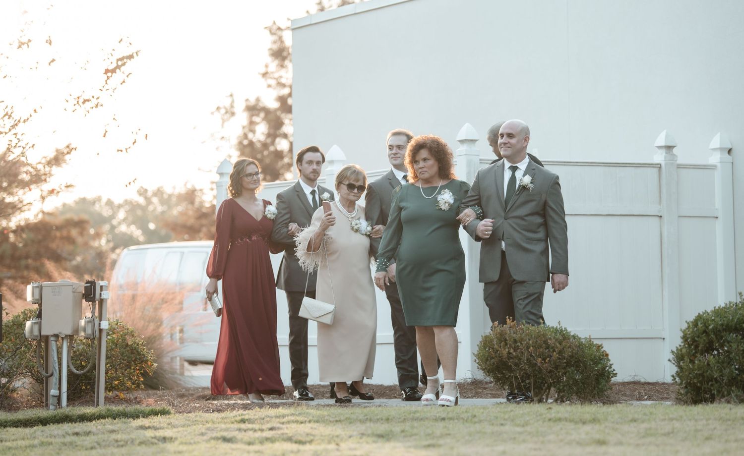 Wedding guests gather outside a white building during golden hour at a sunset ceremony.