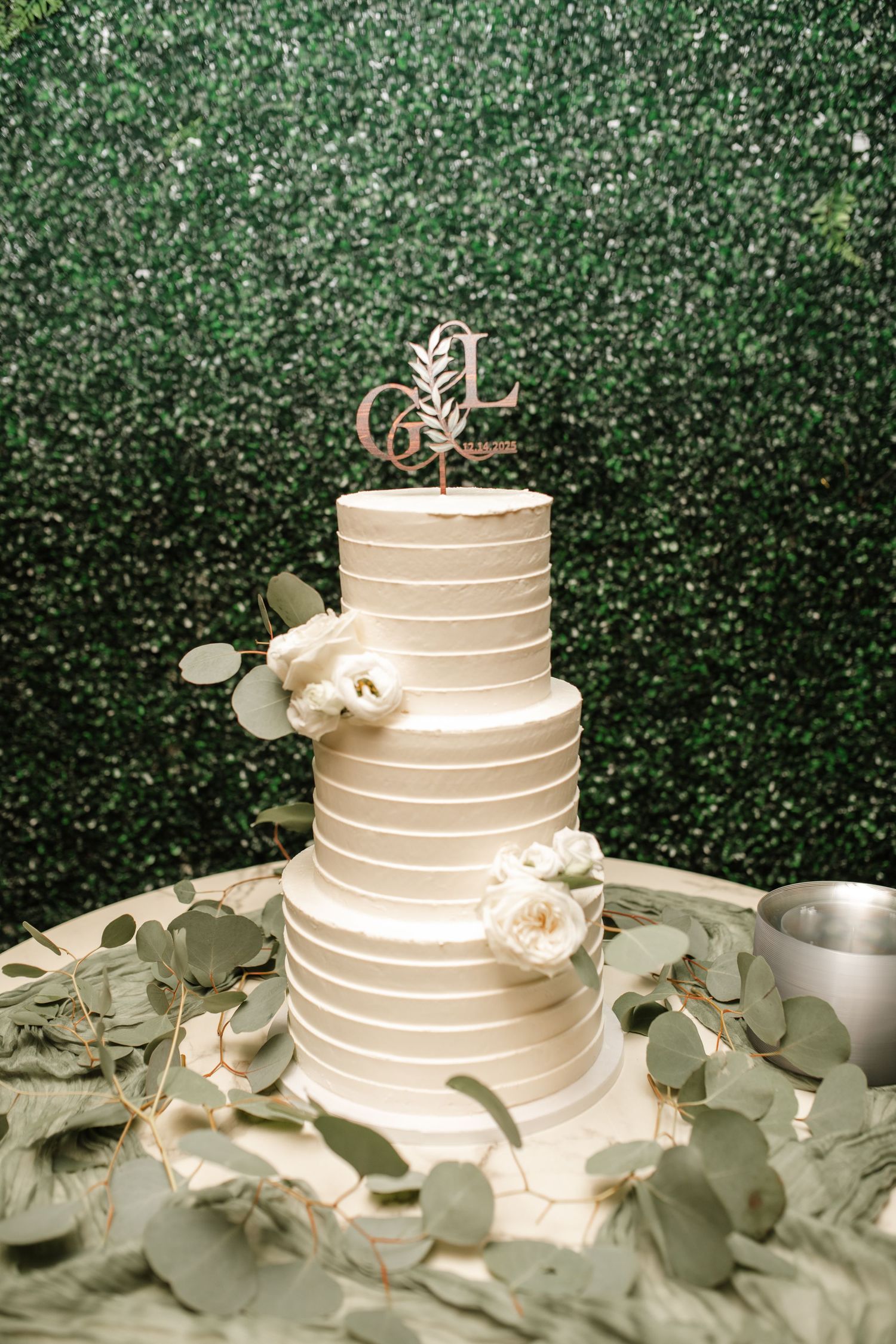Elegant white wedding cake with simple horizontal lines decorated with eucalyptus and roses.