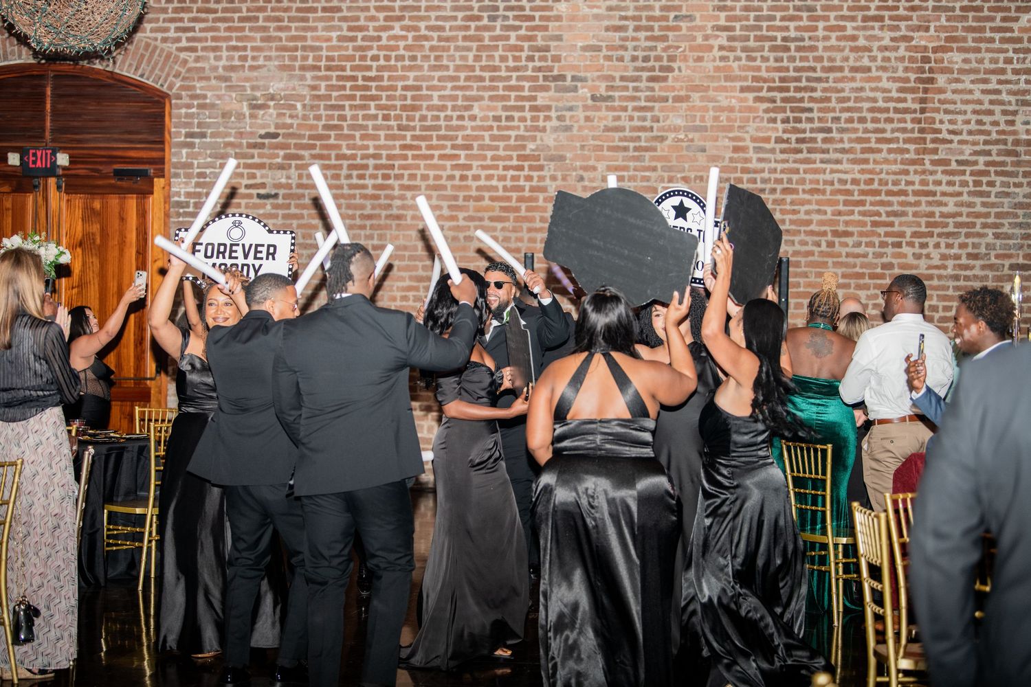 Lively dance party at wedding reception with exposed brick backdrop.