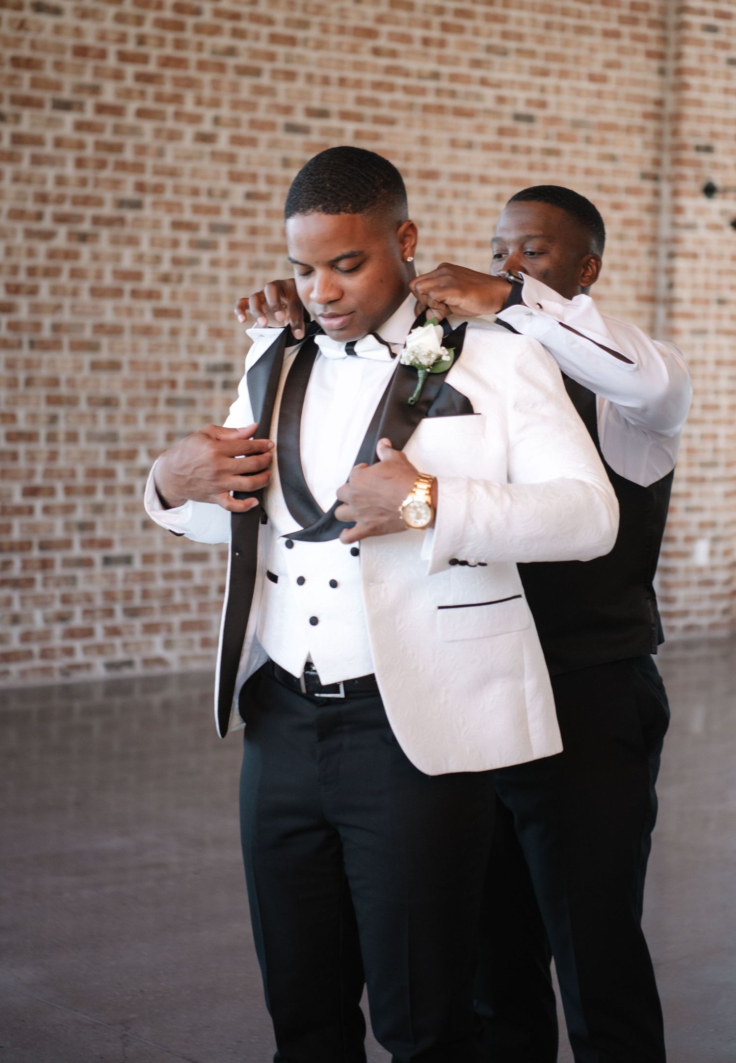 Wedding party members assist each other with formal attire preparations.