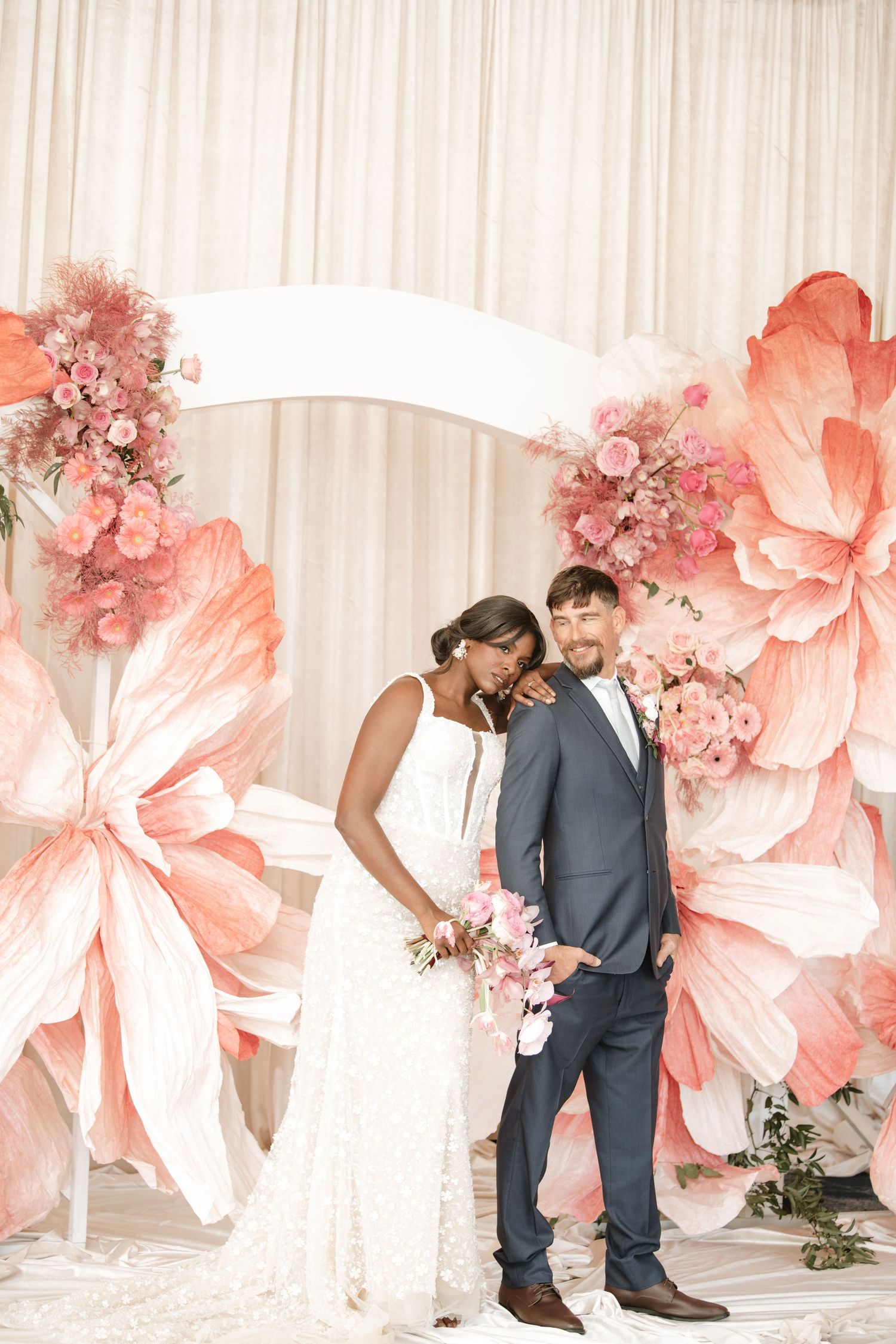 Wedding couple shares intimate moments in front of a coral paper flower wall.