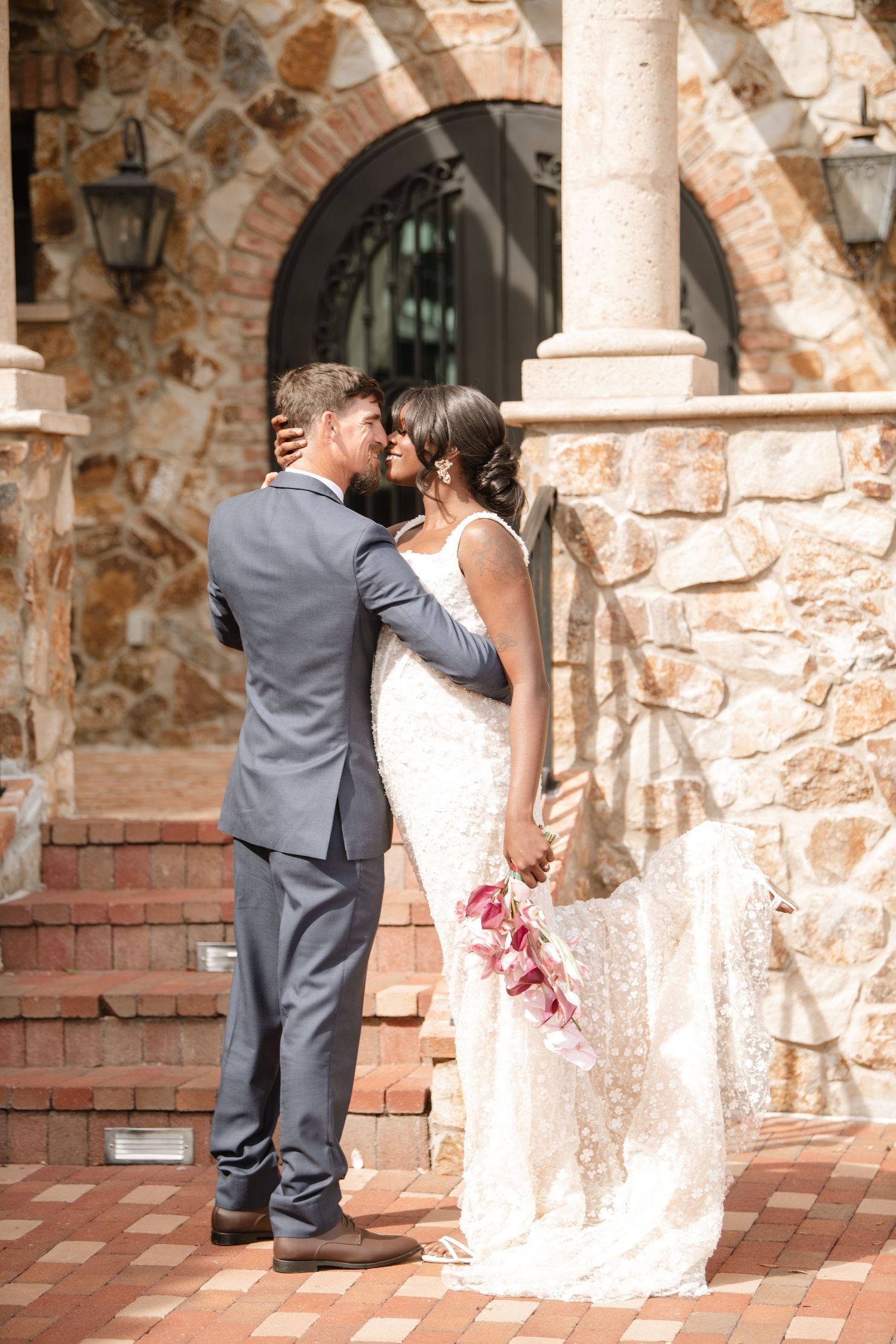 Newlyweds embrace near stone pillars at rustic venue.
