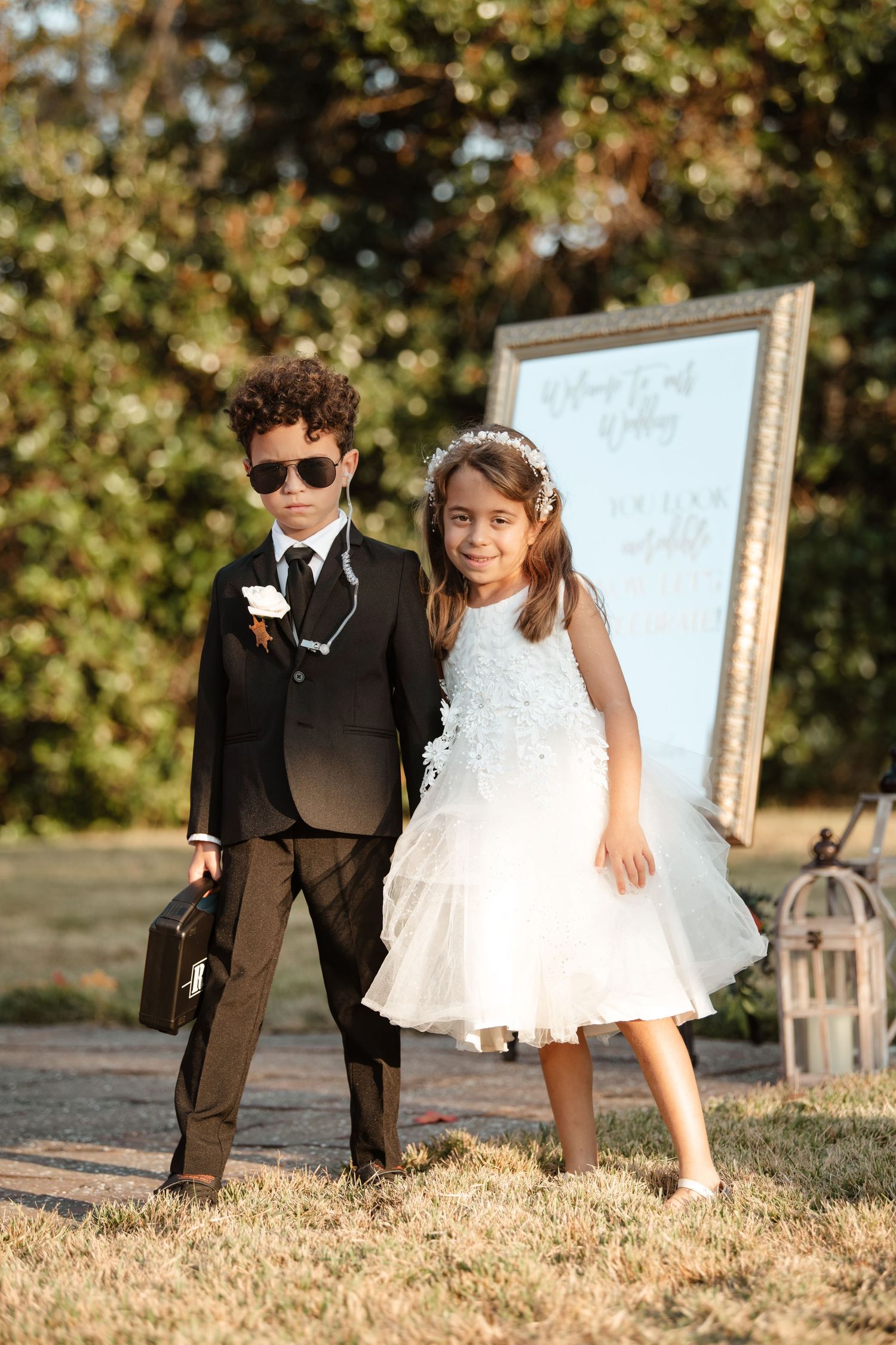 Two young children in formal attire playing near decorative mirrors outdoors.