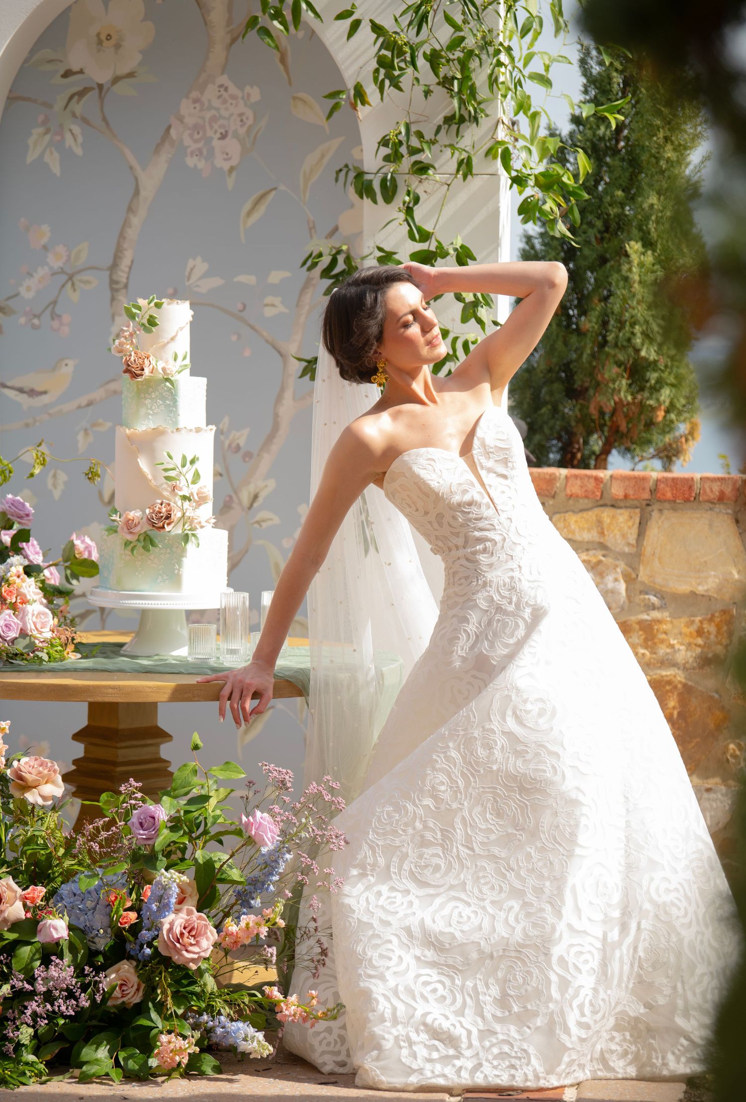 Elegant lace wedding dress with flowing train displayed in a garden setting with pink roses and greenery.
