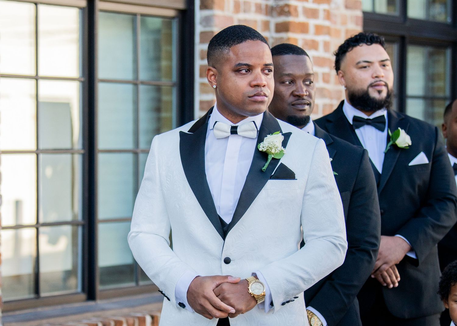 Groomsmen in formal attire pose against a brick wall backdrop.