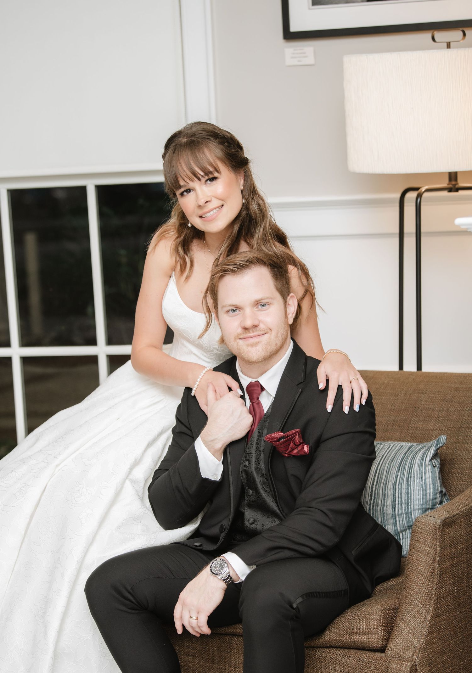 Couple relaxes together on brown couch during wedding photoshoot.