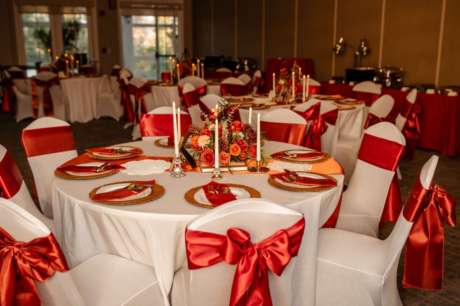 Wedding reception tables decorated with elegant white linens and red satin bows.
