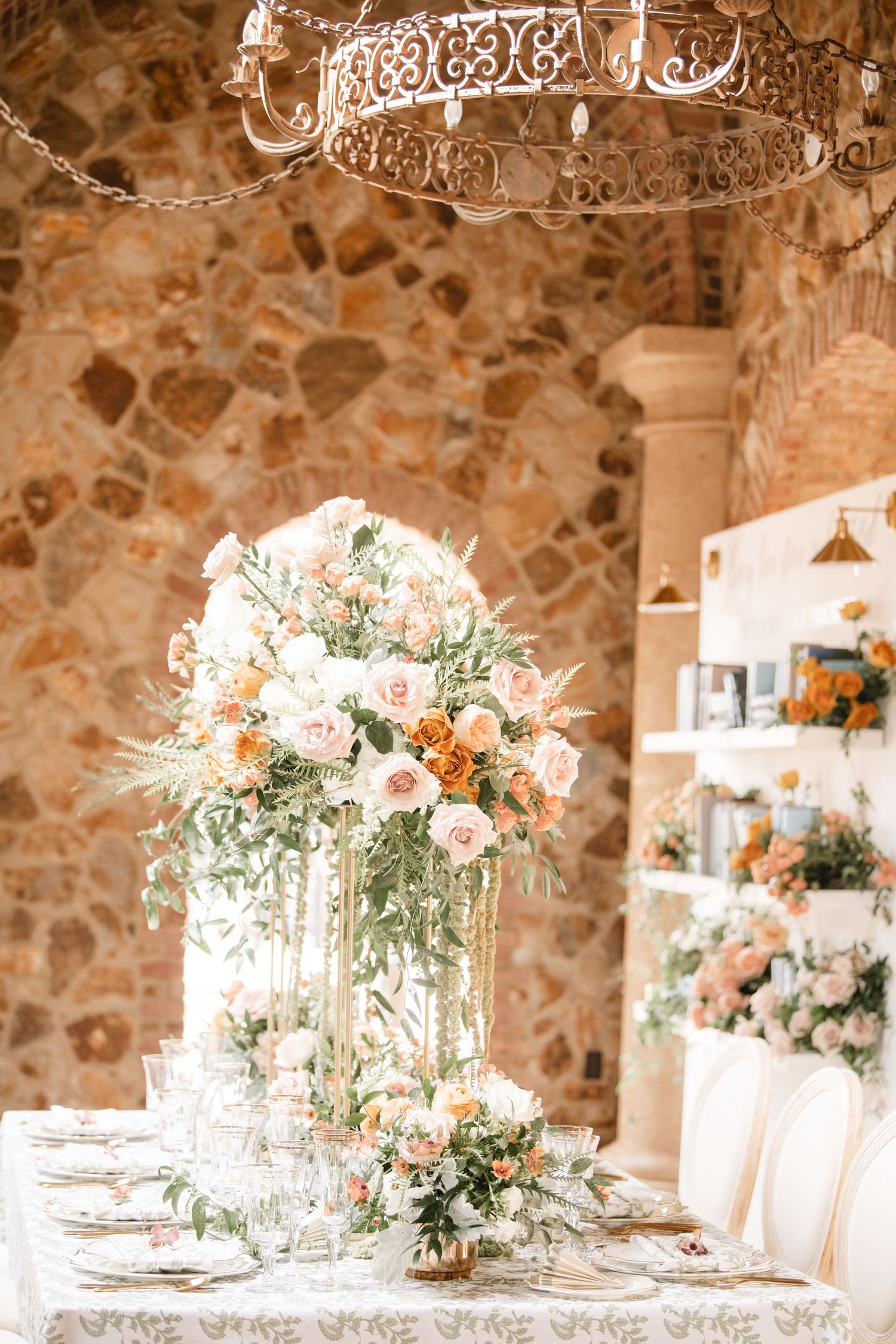 Rustic stone venue with elegant table settings and tall floral centerpieces for a wedding reception.
