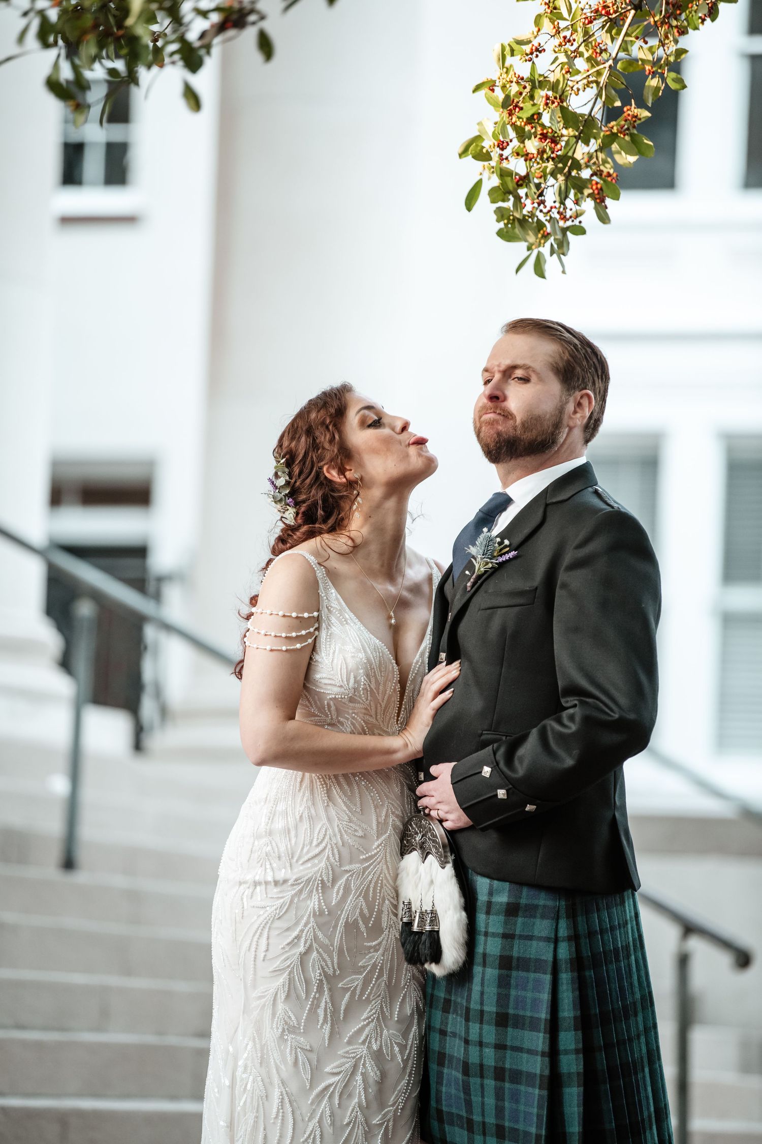 A couple shares a joyful moment in formal wedding attire with the groom wearing a traditional Scottish kilt.