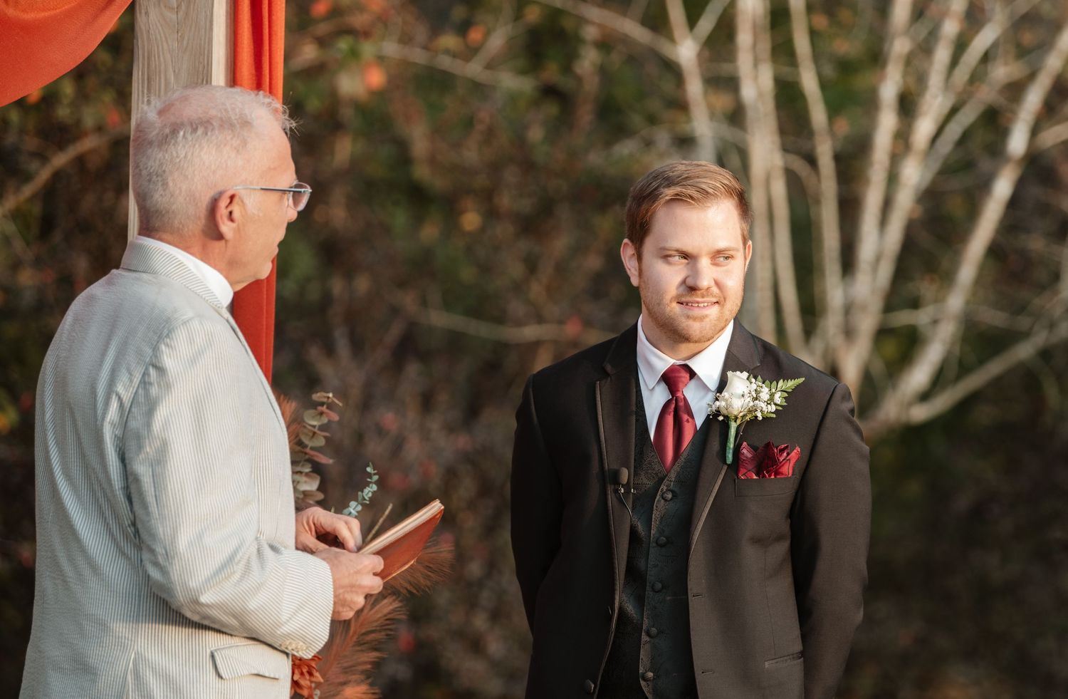 Two people stand together under an orange draped arch at an outdoor ceremony.